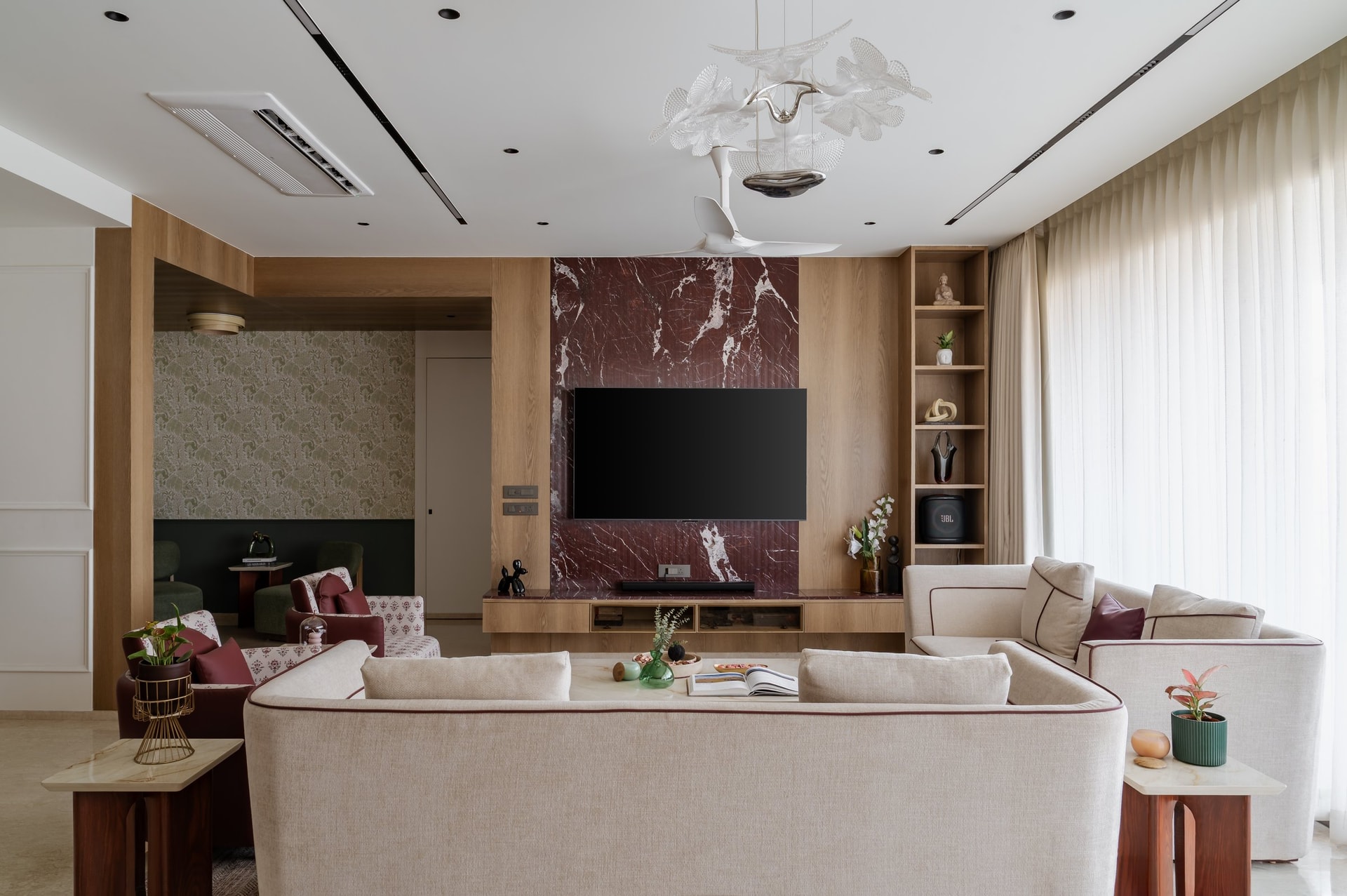 The living room, anchored by an oxblood marble media wall veined in white against warm oak panelling