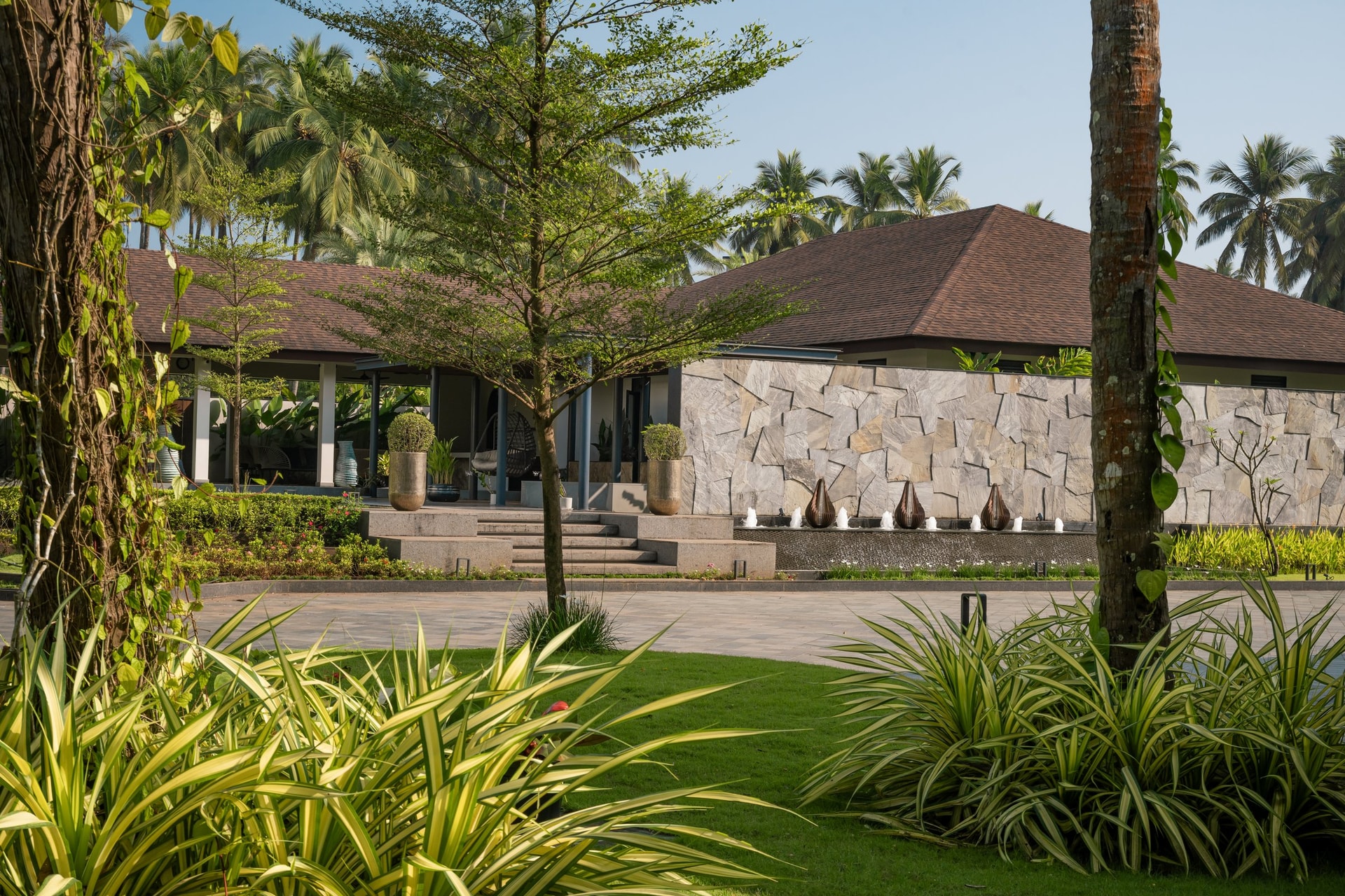 A rubble-stone wall and slender bronze water features extend the architecture into the garden approach
