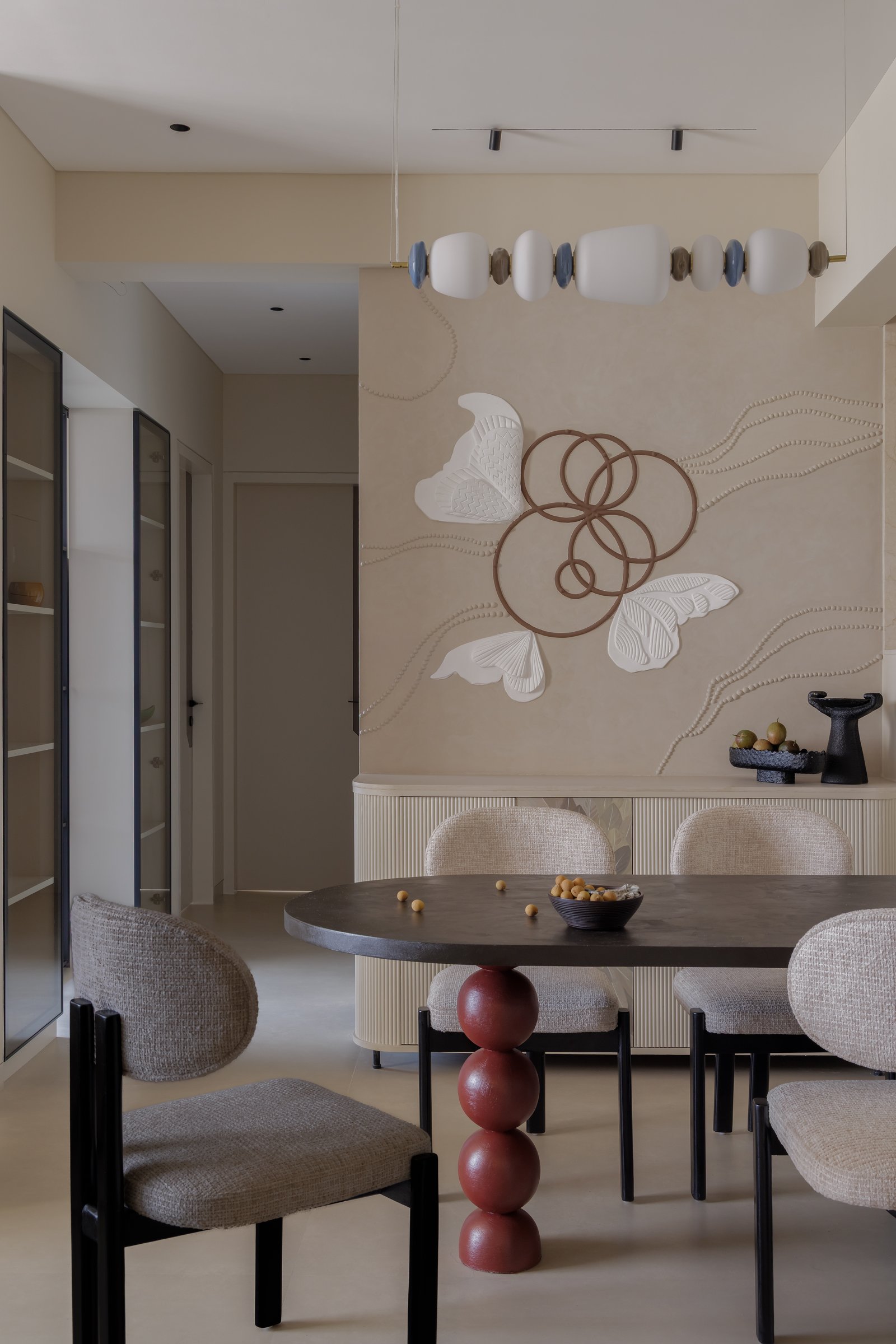 The dining area, where an oval table on a stacked oxblood pedestal sits beneath a beaded relief mural of butterflies and copper rings