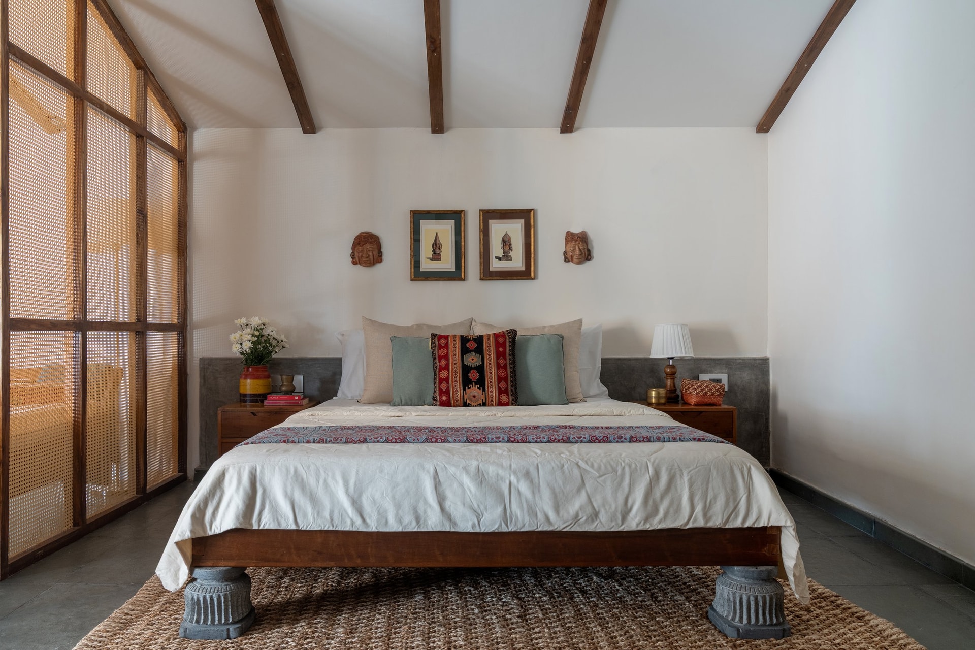 The bedroom, where a custom Pillai Maruthu bed with fluted stone temple-base legs sits beneath a sloping ceiling of exposed teak rafters