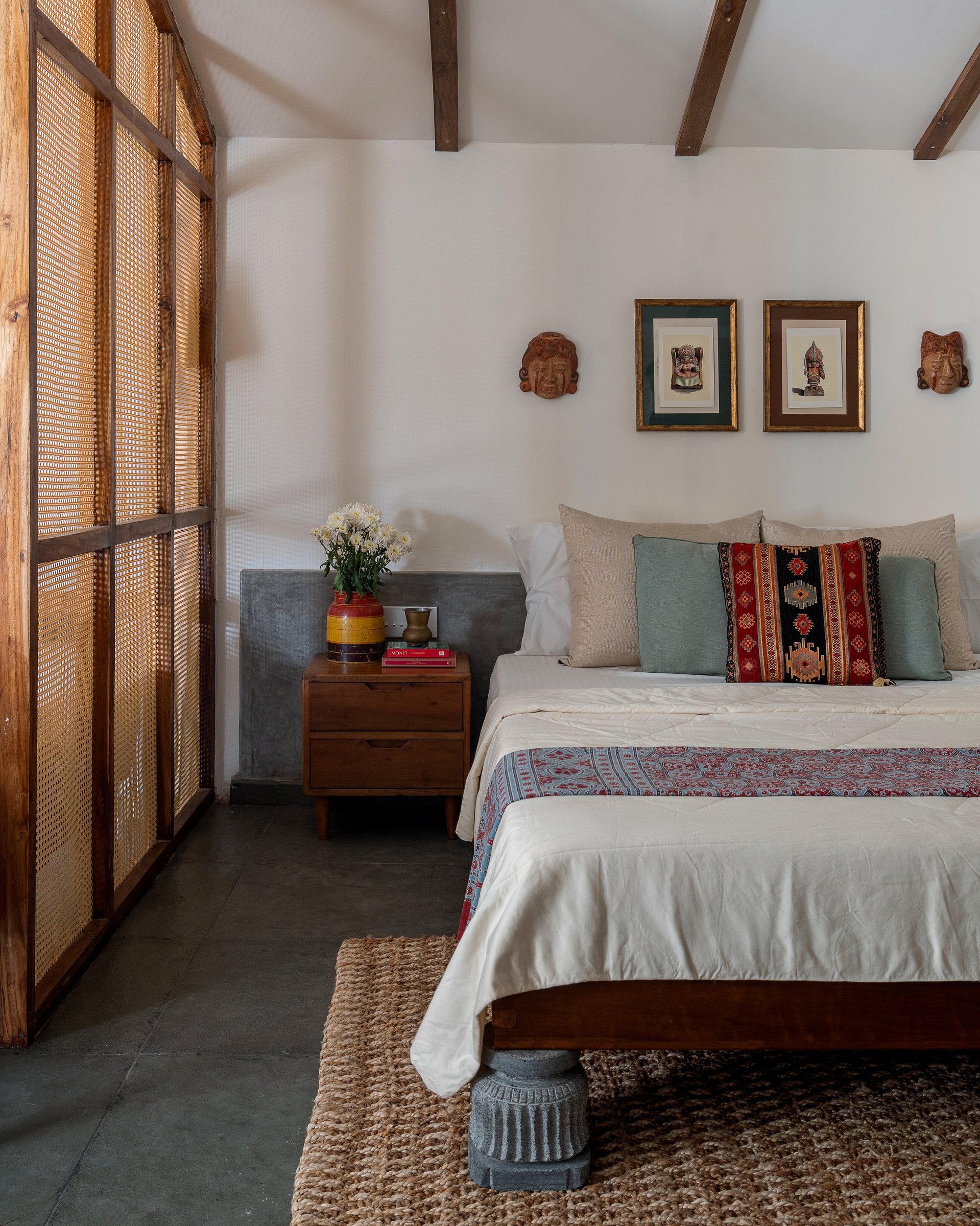 The bedroom, where a mid-century bedside table and a pair of terracotta masks give the wall above the bed its cultural register