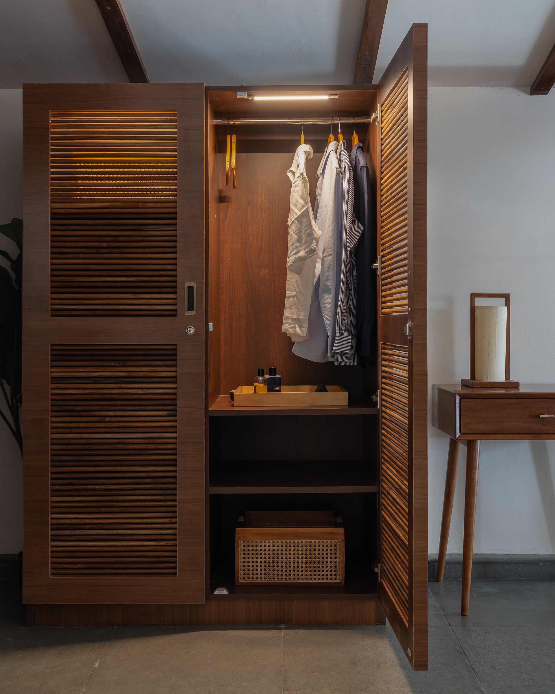 The wardrobe, opened to reveal sensor-operated interior lighting and a teak-lined shelf below the hanging bay