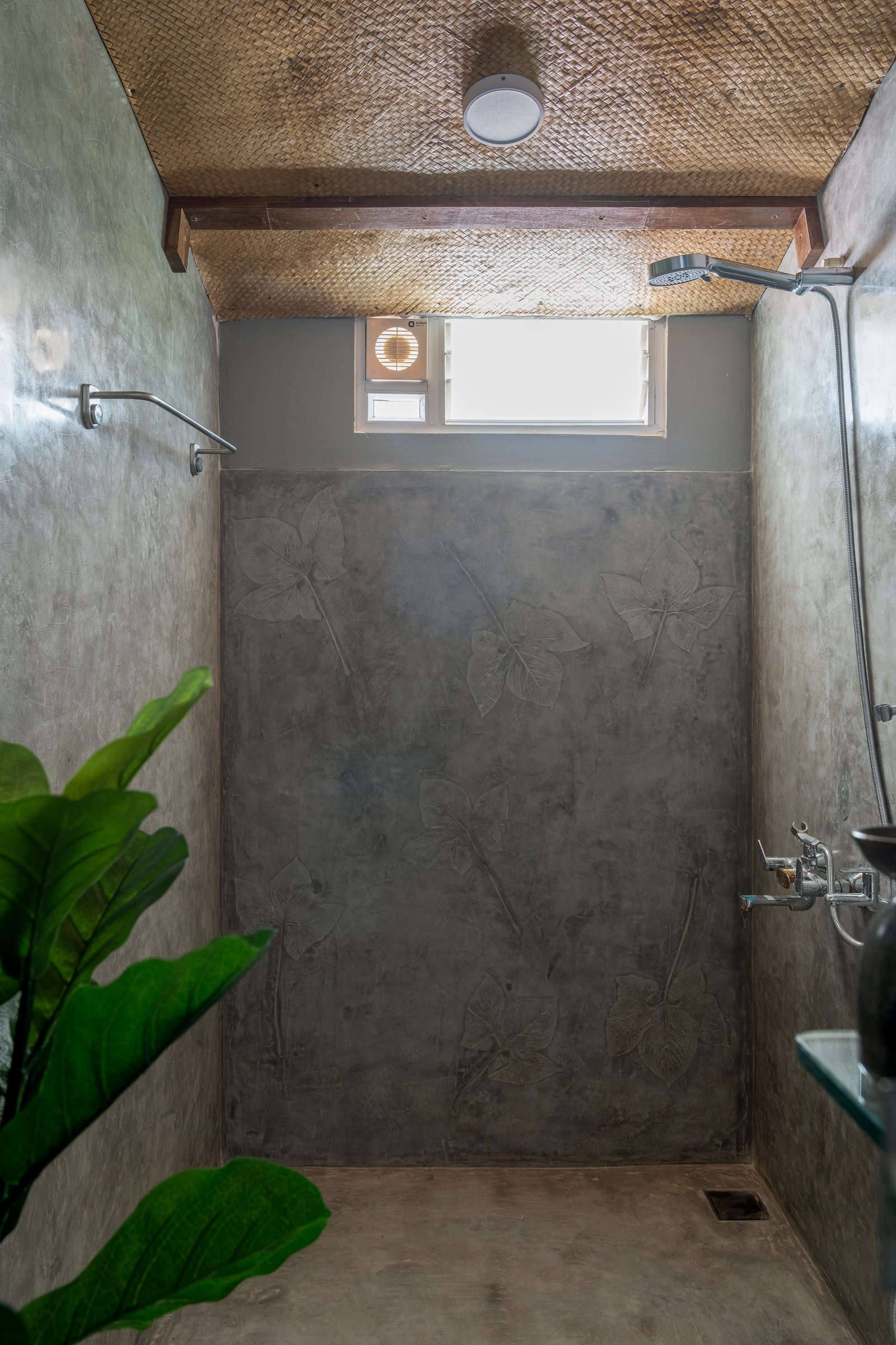 The shower, where leaf outlines have been hand-etched into an oxide plaster wall beneath a woven bamboo ceiling