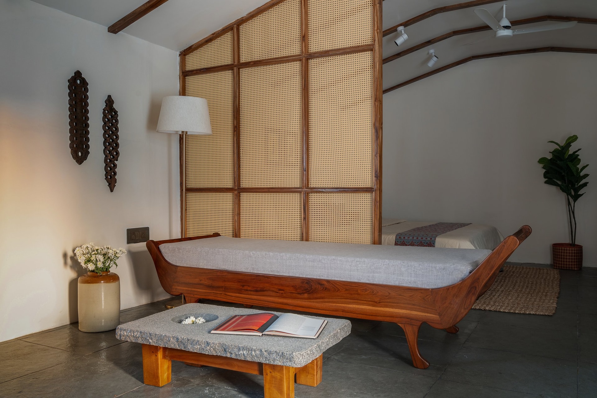 The living area, where a handcrafted hardwood diwan and a chiselled granite coffee table set the home's material register against a full-height cane-and-wood partition