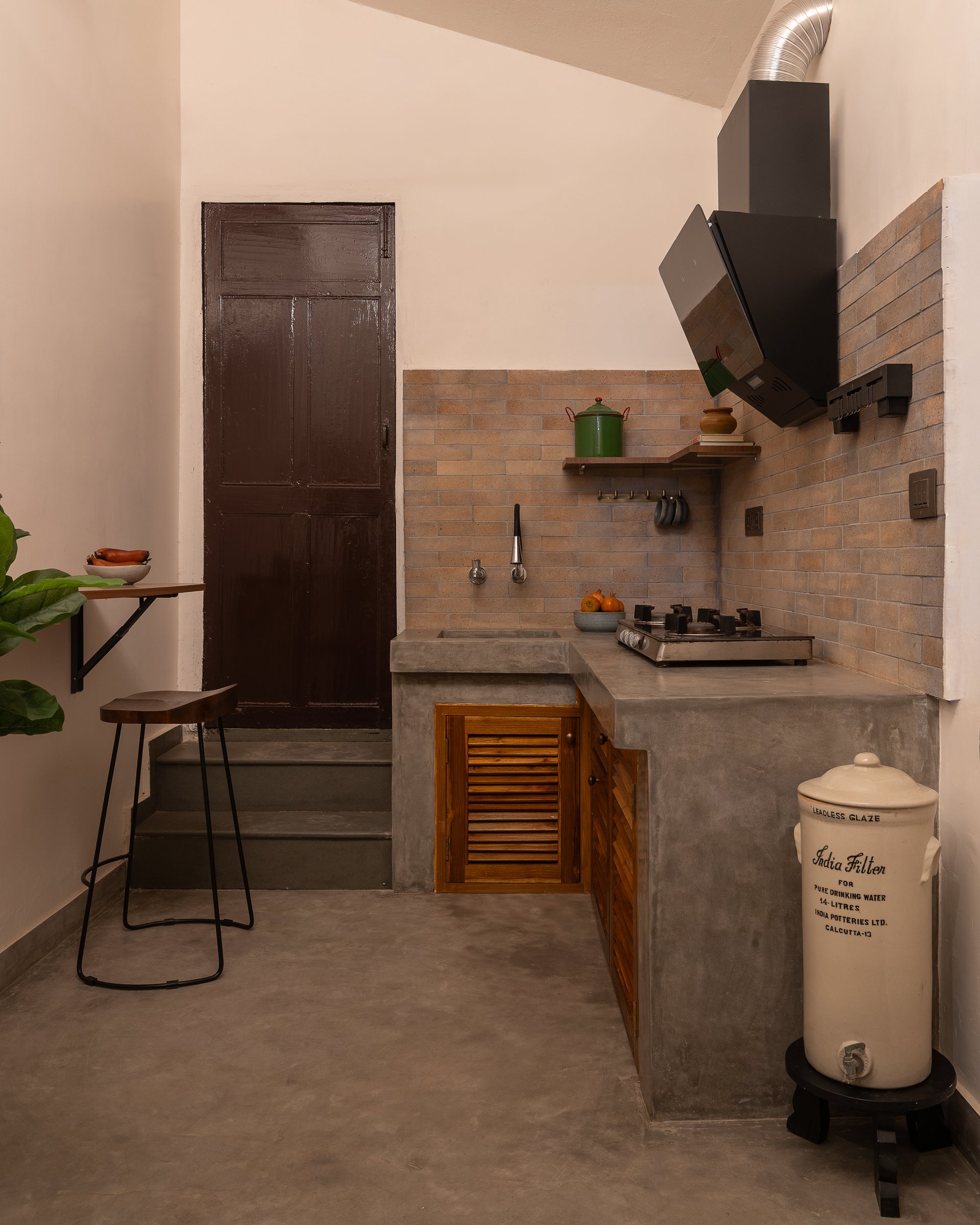 The kitchen, where grey oxide counters meet an exposed brick backsplash in a compact L-shaped run