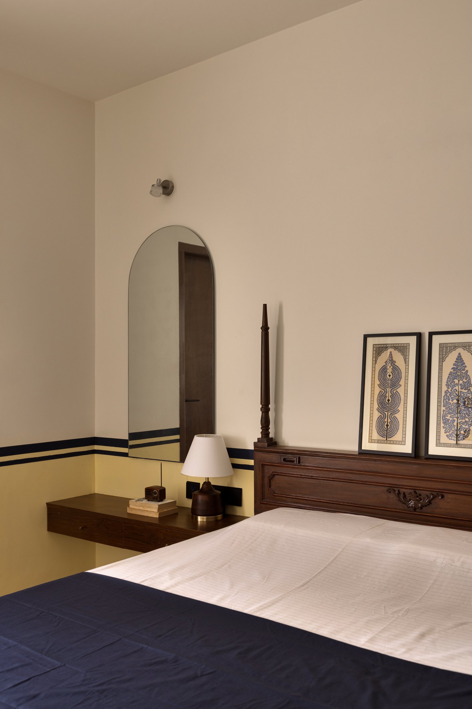The master bedroom, where bands of yellow and navy meet a rosewood headboard and framed folk artworks in indigo