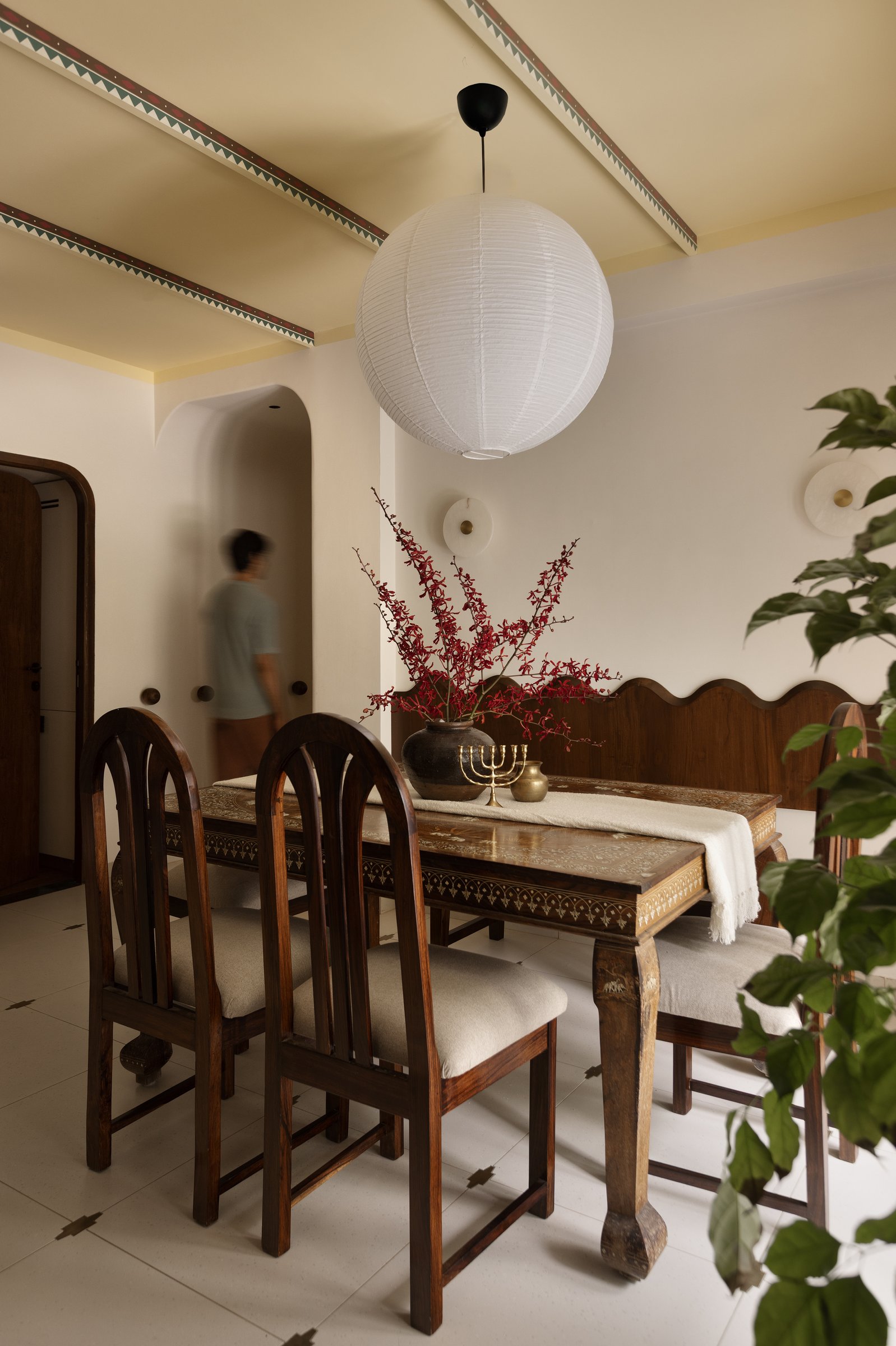 The dining room's wave-backed bench, a contemporary reading of traditional craftsmanship beneath a plain paper globe lantern
