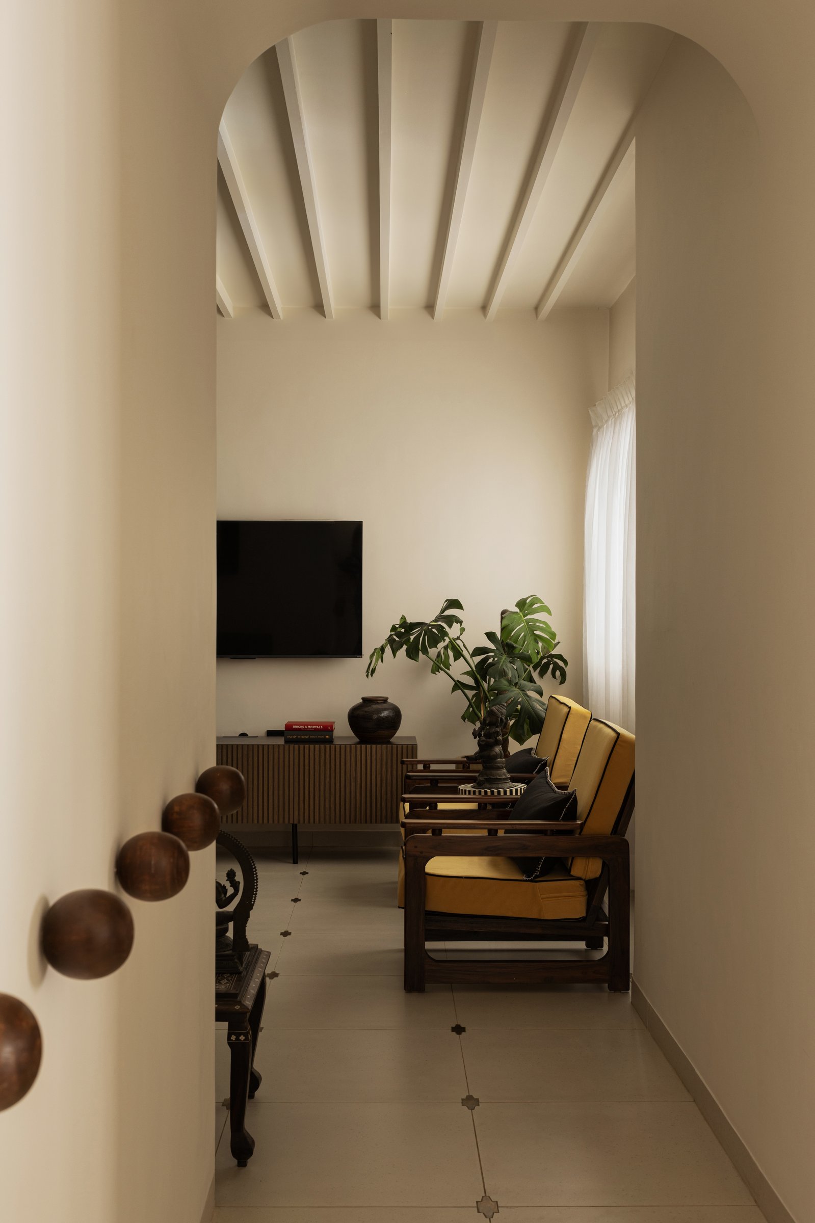 The view from the passage, where an arched opening frames the living room and wooden spheres run along the wall as a sculptural handrail