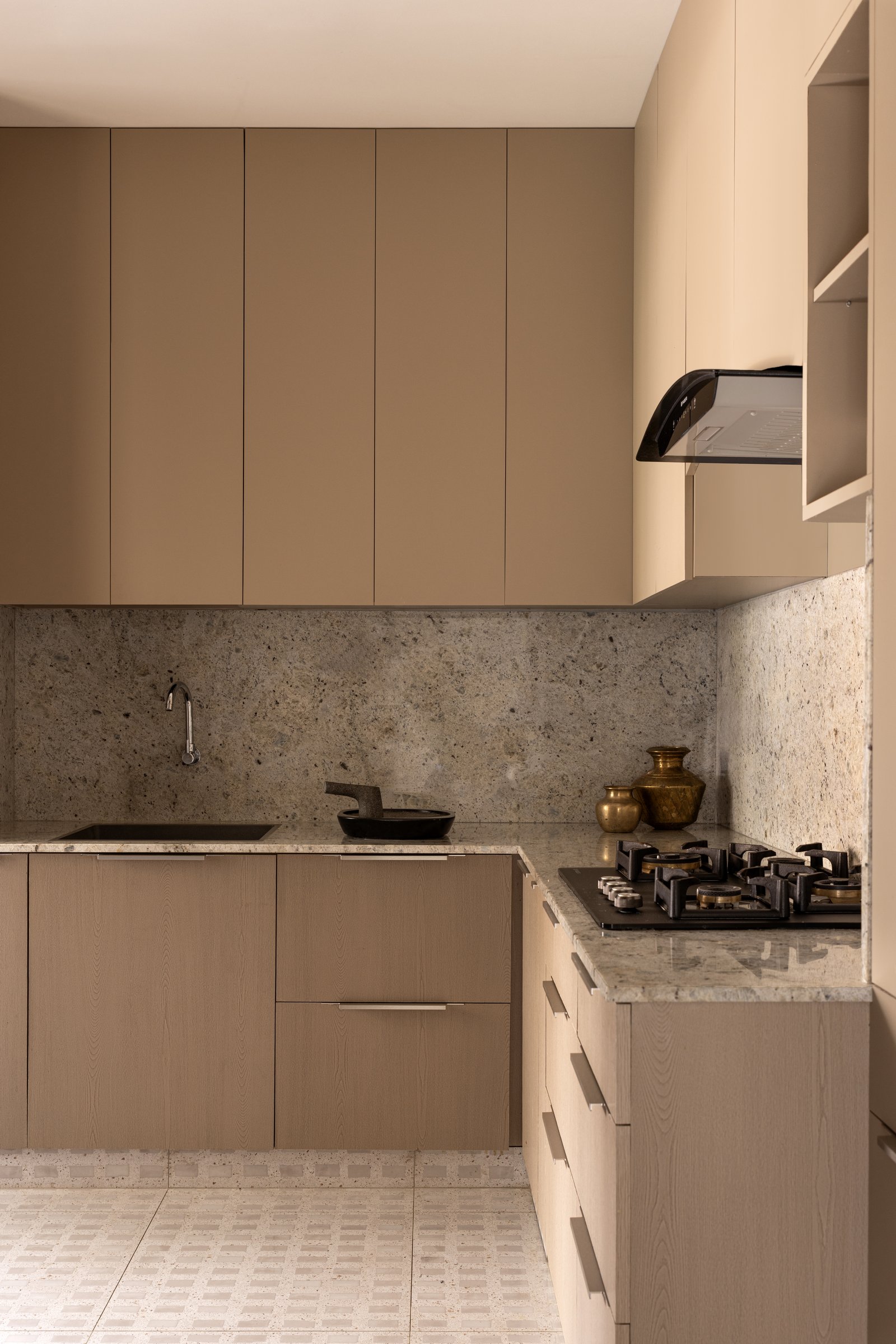 The kitchen, where warm taupe cabinetry meets a veined granite counter and a pair of heirloom brass vessels