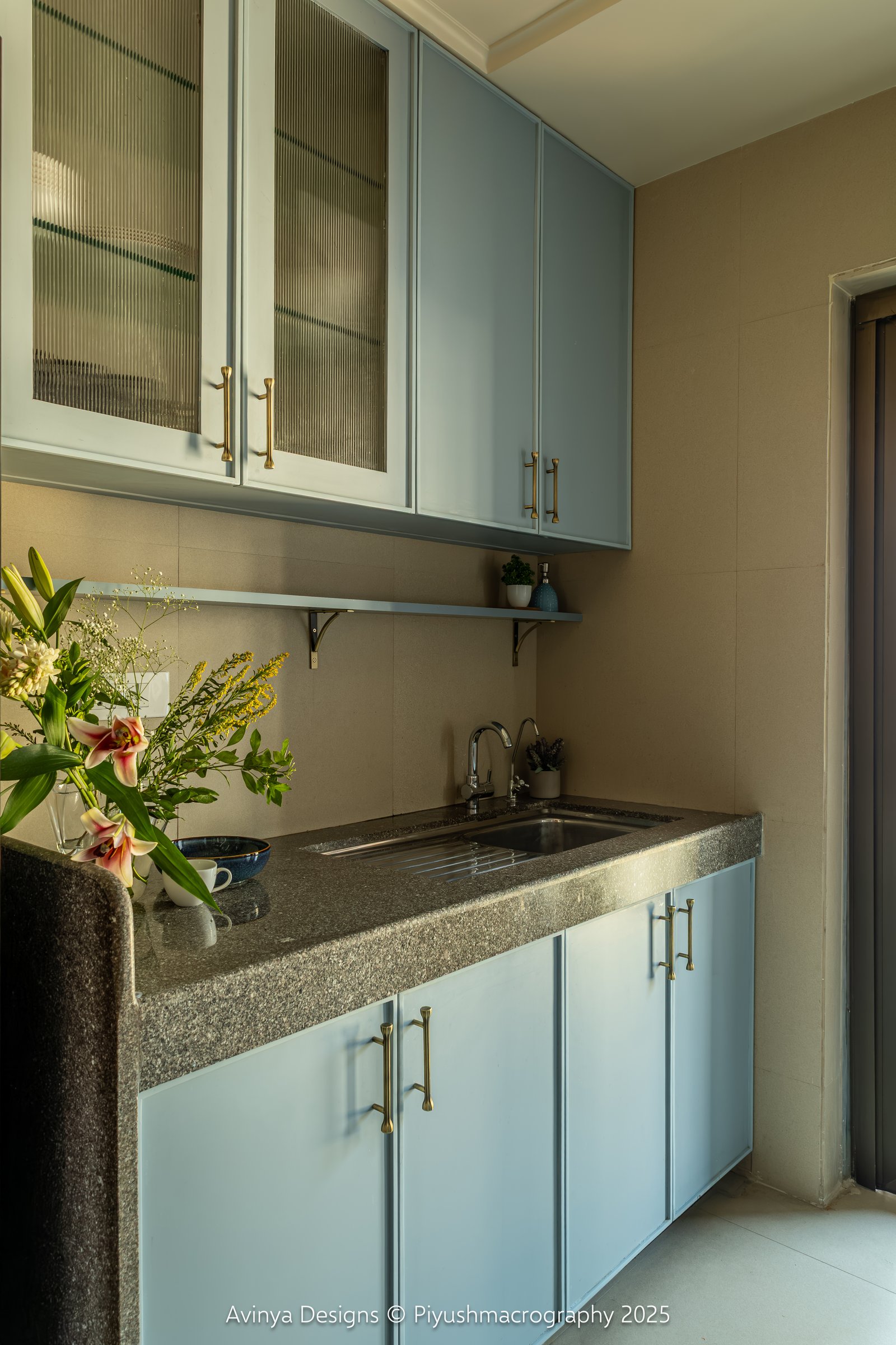 The utility counter, where reeded glass fronts and a floating shelf resolve the sink zone against a warm taupe tile wall