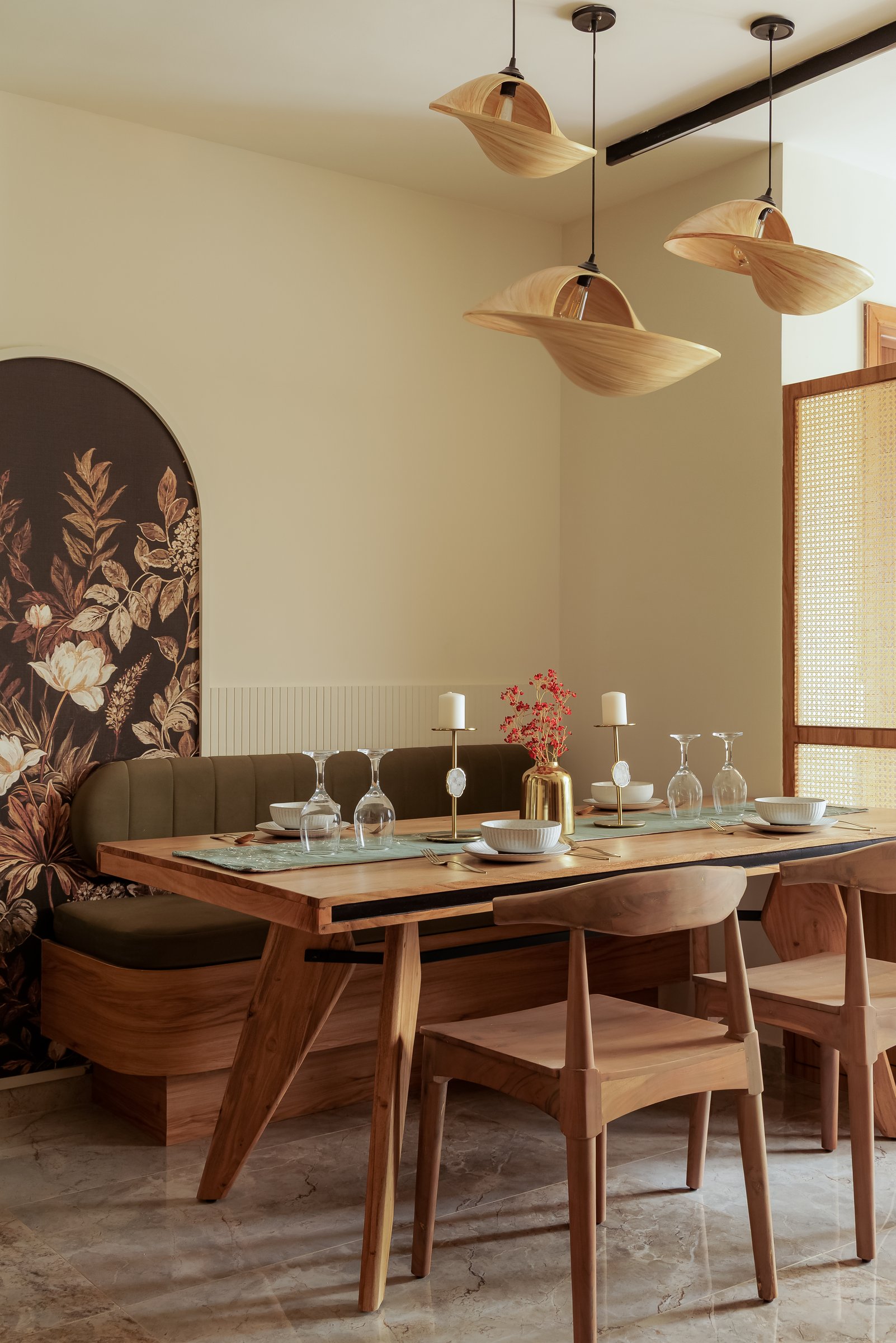 The dining area, where a handcrafted wooden table and olive banquette are gathered beneath a cluster of woven pendants