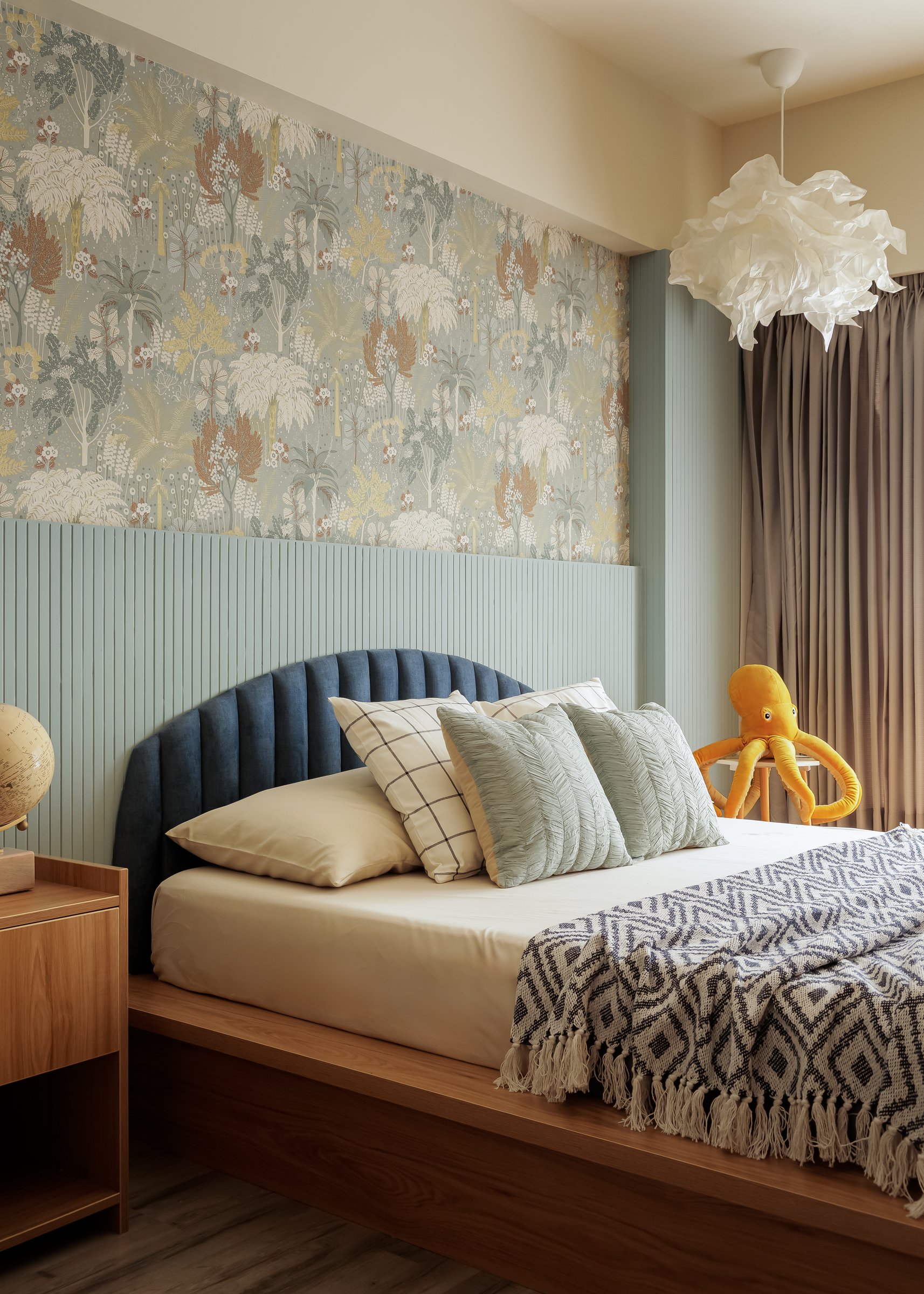 The child's bedroom, where a nature-inspired wallpaper meets a fluted pale blue-green panel behind a tufted deep blue headboard