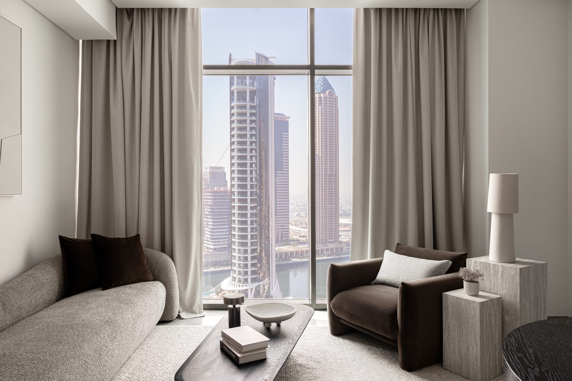 The reason for the palette: a floor-to-ceiling window onto the Business Bay canal, framing the towers the studio built the interior to converse with.