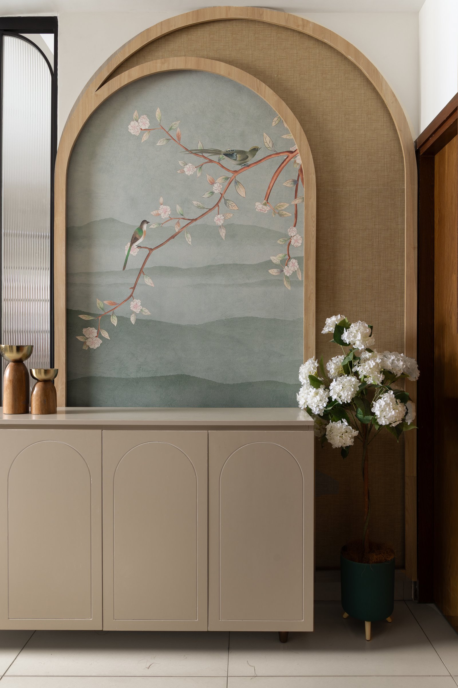 The foyer, where a custom arched surround frames a botanical wallpaper of birds on a flowering branch, setting the home's tonal register at the threshold