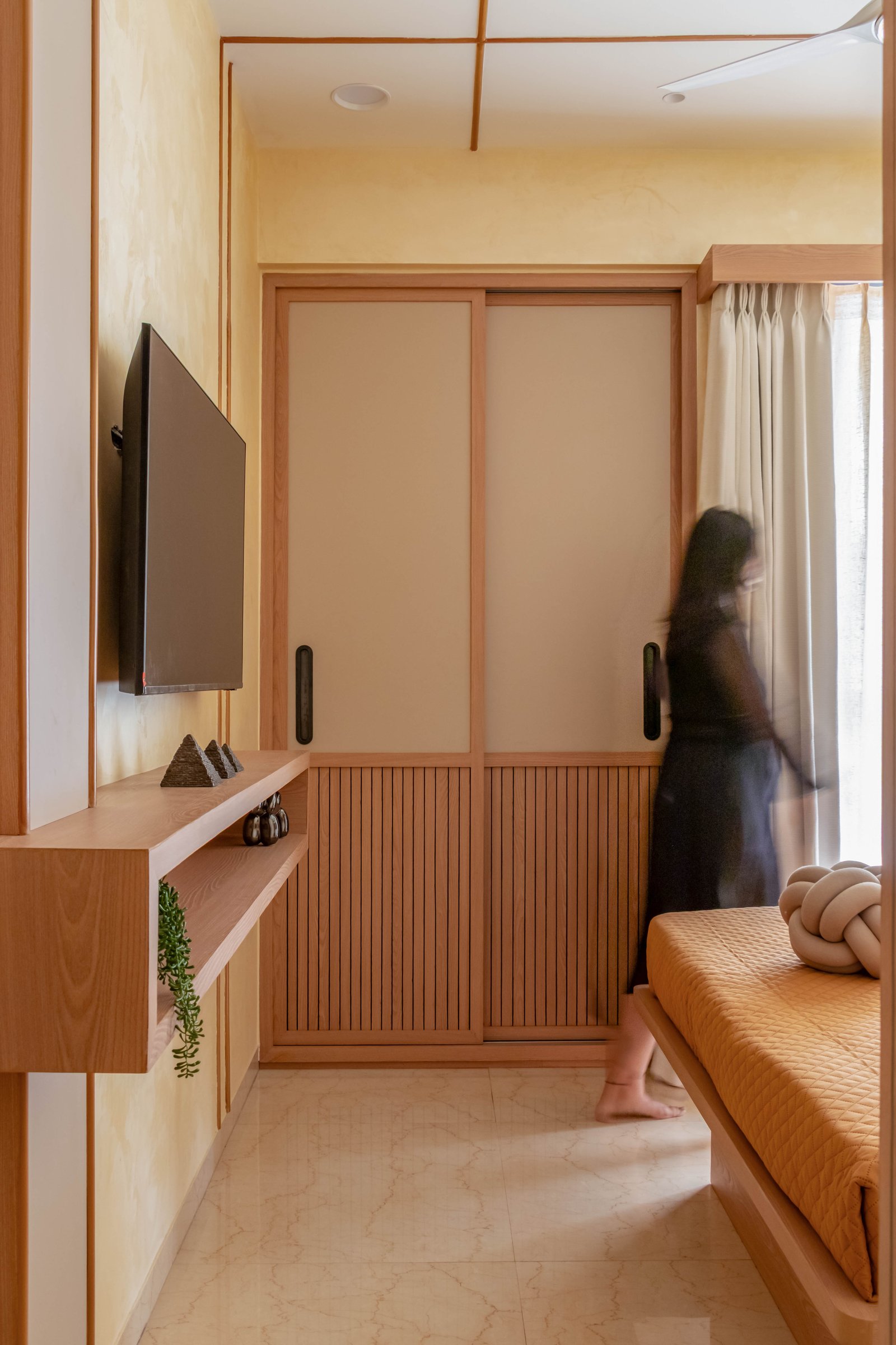 The media wall opposite the bed, where frosted sliding doors and slatted wood cladding carry the Japandi lineage most directly