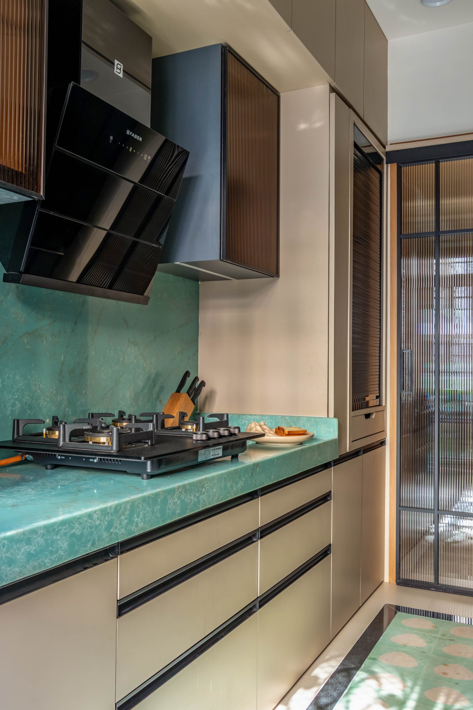 The kitchen, where a veined green stone counter and reeded-glass upper cabinets establish a distinct working register