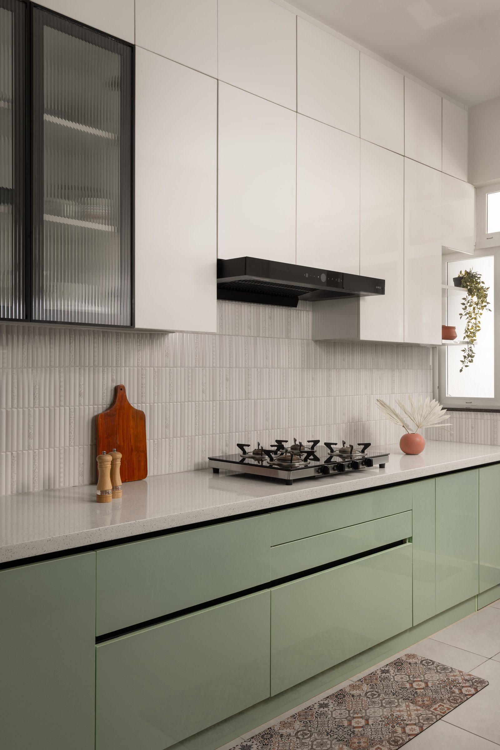 The parallel kitchen, where sage-green base cabinets ground the room and crisp white uppers draw the eye upward, bridged by a fluted white tile backsplash