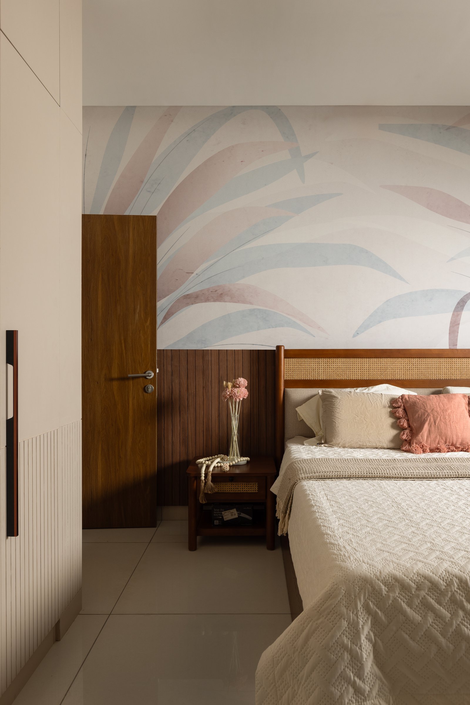 The master suite, its watercolour palm mural paired with lower wood panelling and a cane-inset headboard, resolving the home's Japandi influence