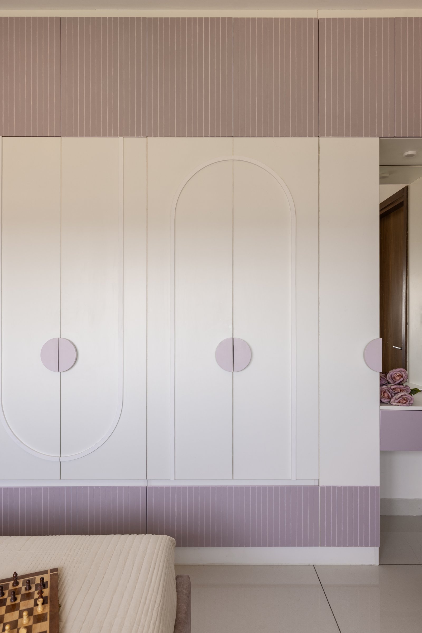 The daughter's wardrobe wall, its ivory doors inscribed with an arched inlay motif and framed by bands of mauve and lilac