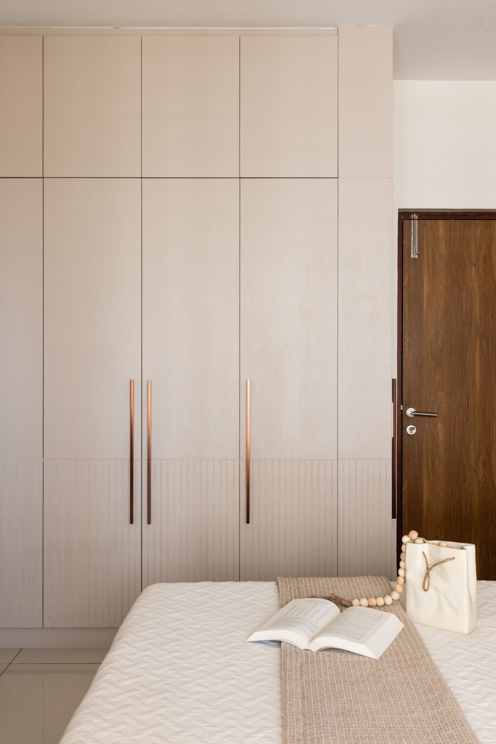 The master wardrobe wall in warm ivory, articulated by slim metallic pulls and a lower band of fluted panelling