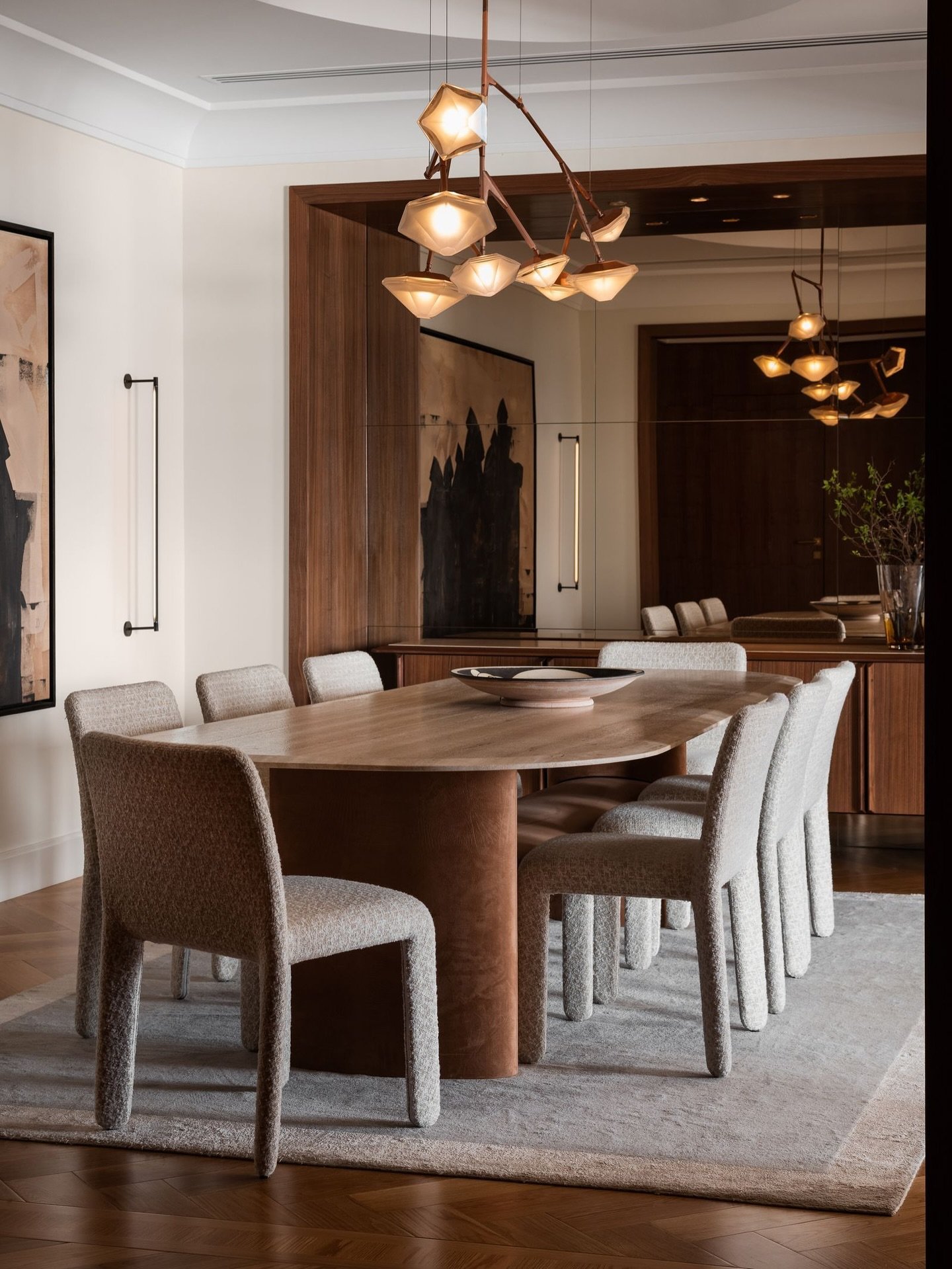 The dining room, anchored by a walnut oval table and a branching brass chandelier.