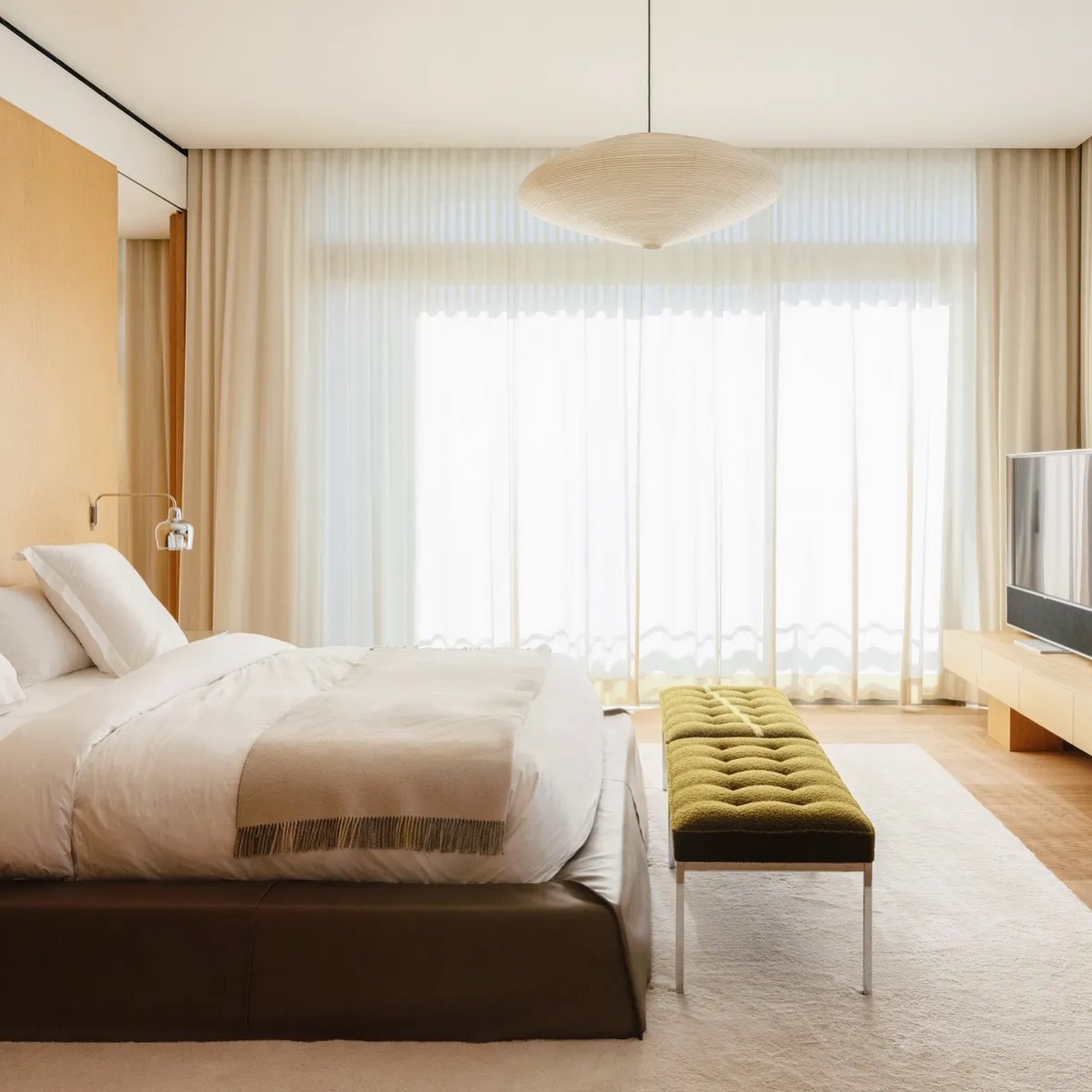 The master suite, wrapped in pale French oak, holds an olive tufted bench as its single strong colour note.