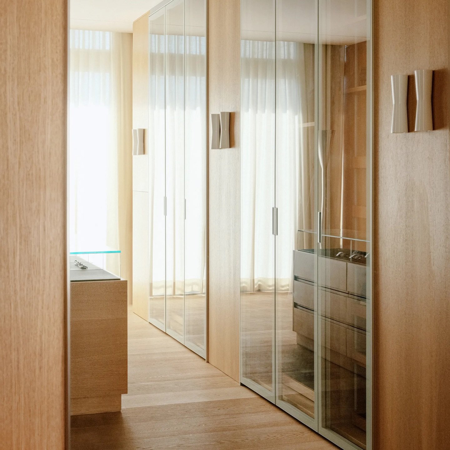 A wood-lined passage opens onto mirrored wardrobe doors that double the daylight and lengthen the space.