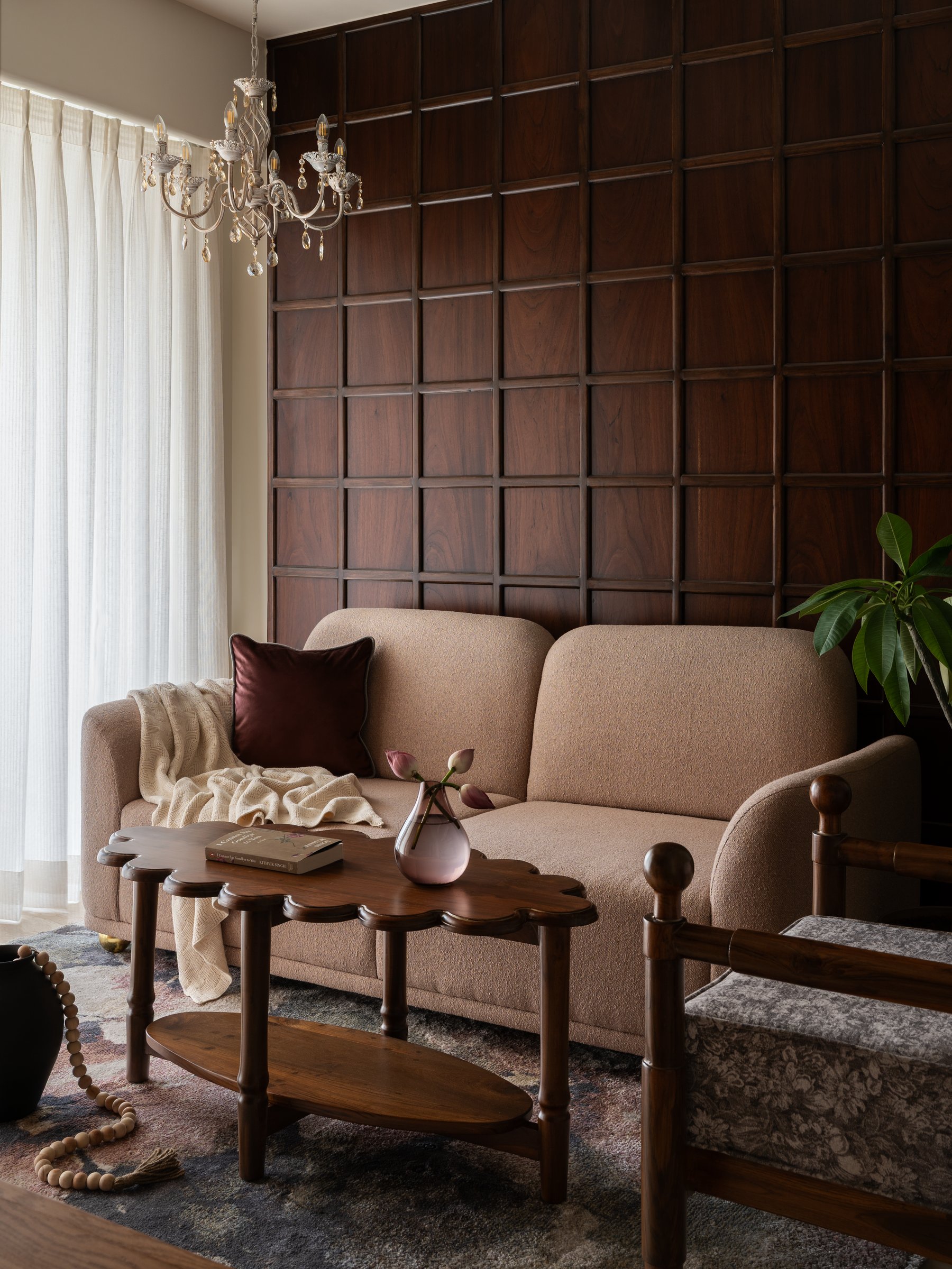 The living room, where a curved bouclé sofa softens the disciplined grid of the teak feature wall behind it