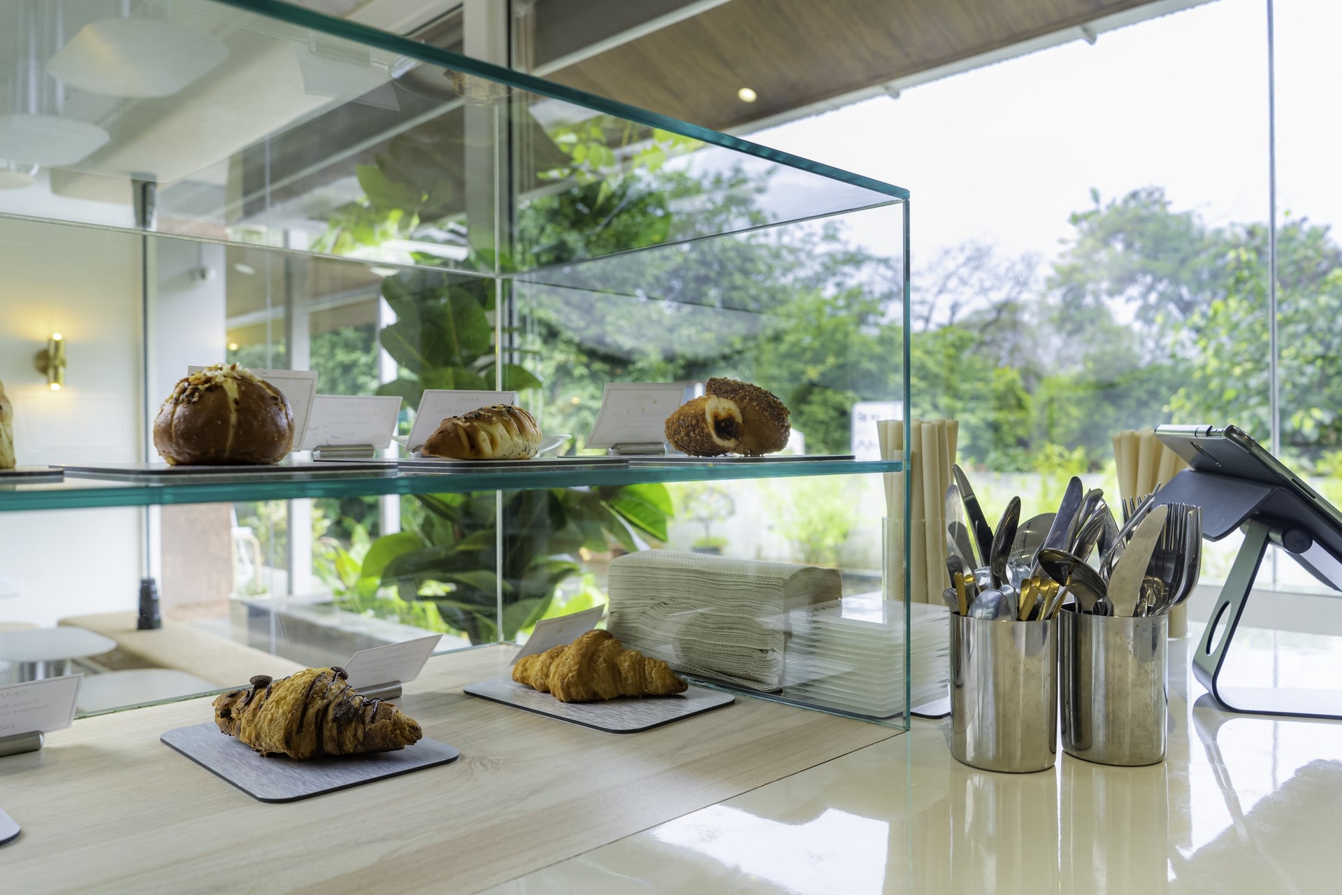 The pastry case, where a frameless glass box holds the morning's viennoiserie against the courtyard greenery