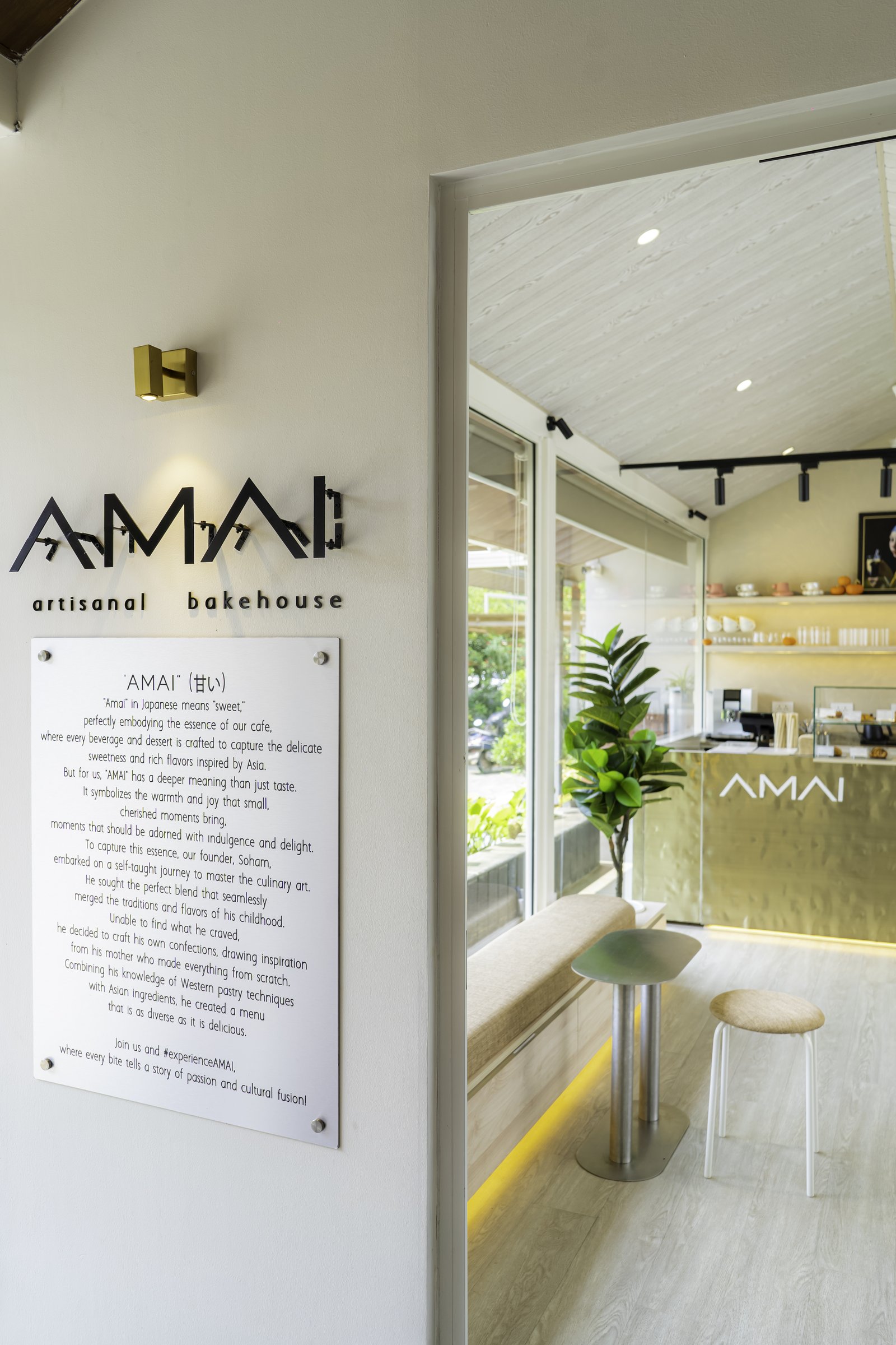 The entry, where the black cut-metal AMAI logotype and a printed narrative panel introduce the café through an open doorway