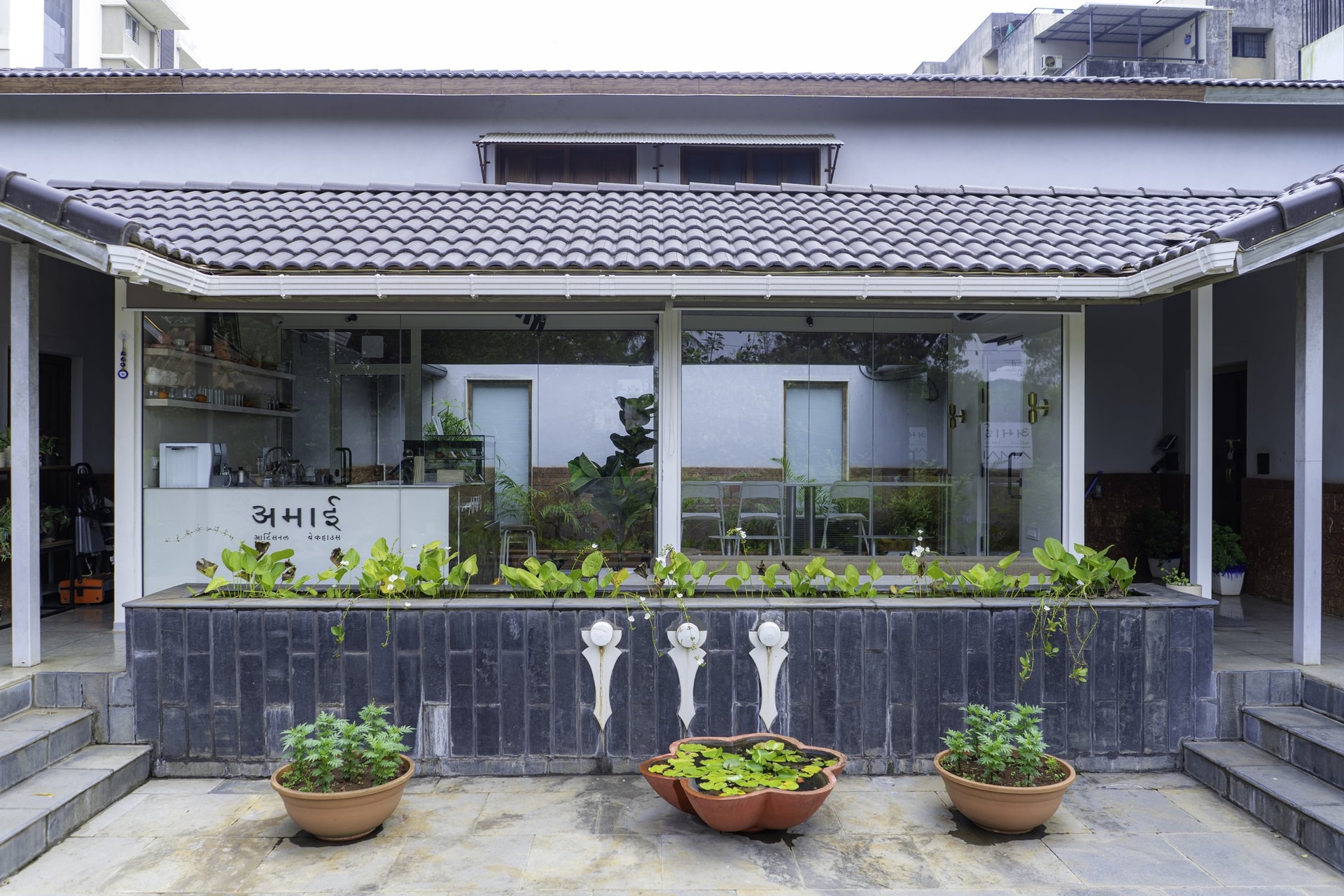 The forecourt elevation, where a tiled pitched roof and a grey brick planter frame the café's fully glazed frontage