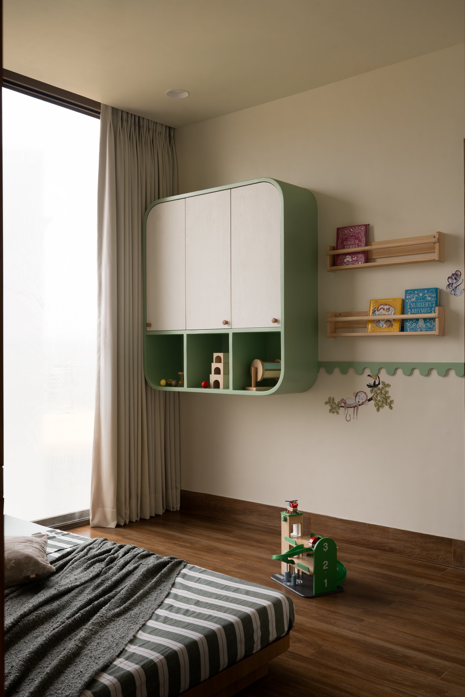 The children's storage wall, its rounded sage-green cabinet holding toys and books with sculptural clarity
