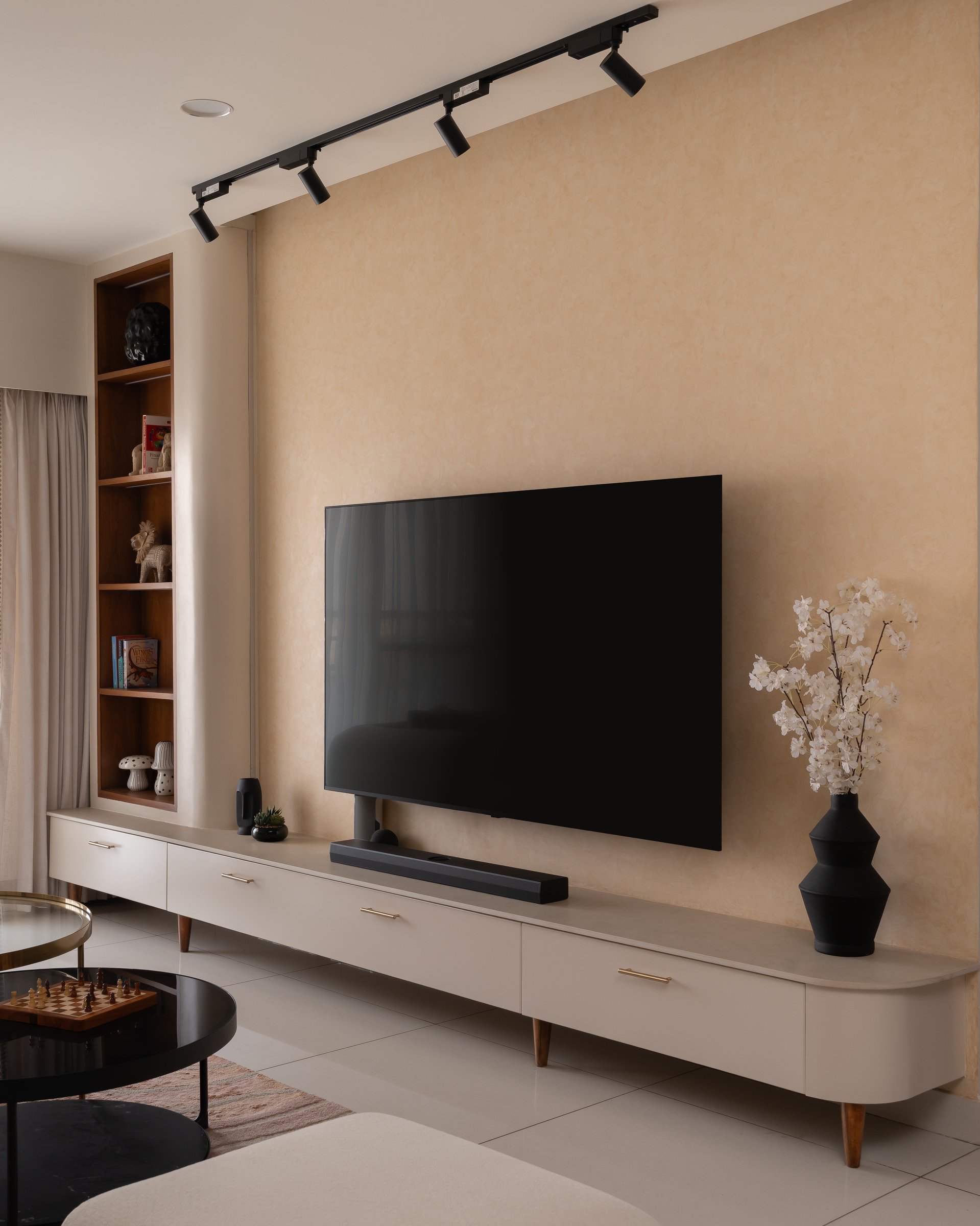 The media wall, where textured ochre plaster and a low ivory console carry the room's ambient glow