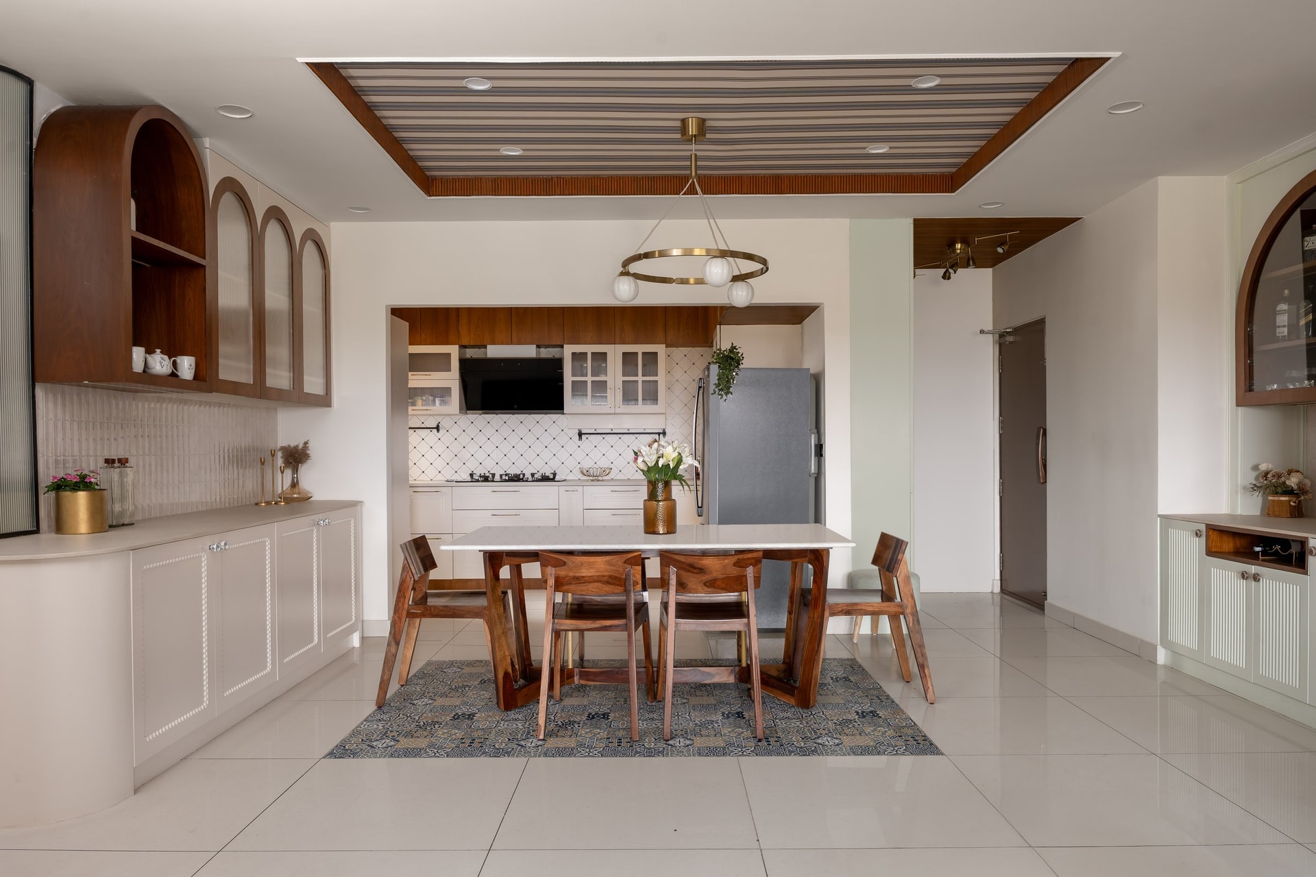 The full dining composition, where arched glass-fronted cabinets flank the table and the kitchen opens beyond