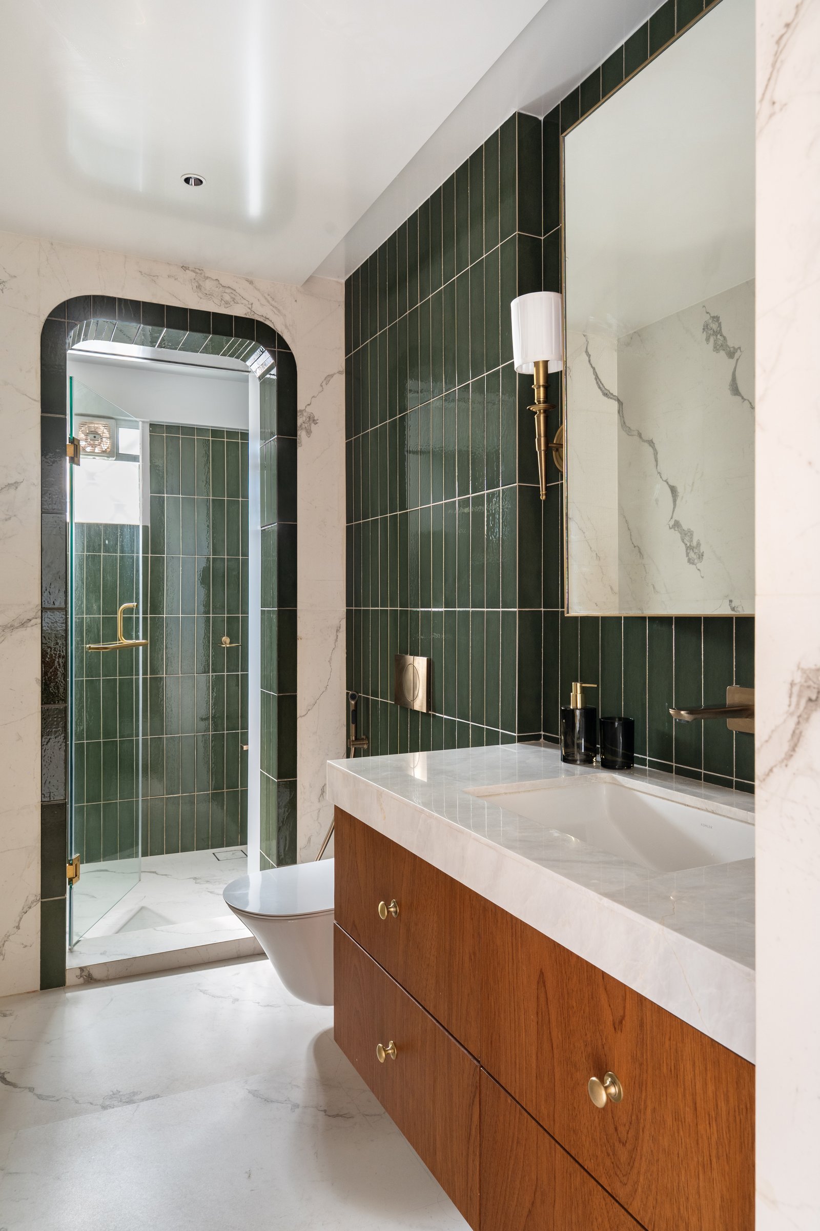 The primary bathroom, where deep green vertical tiles meet veined stone cladding around a floating teak vanity