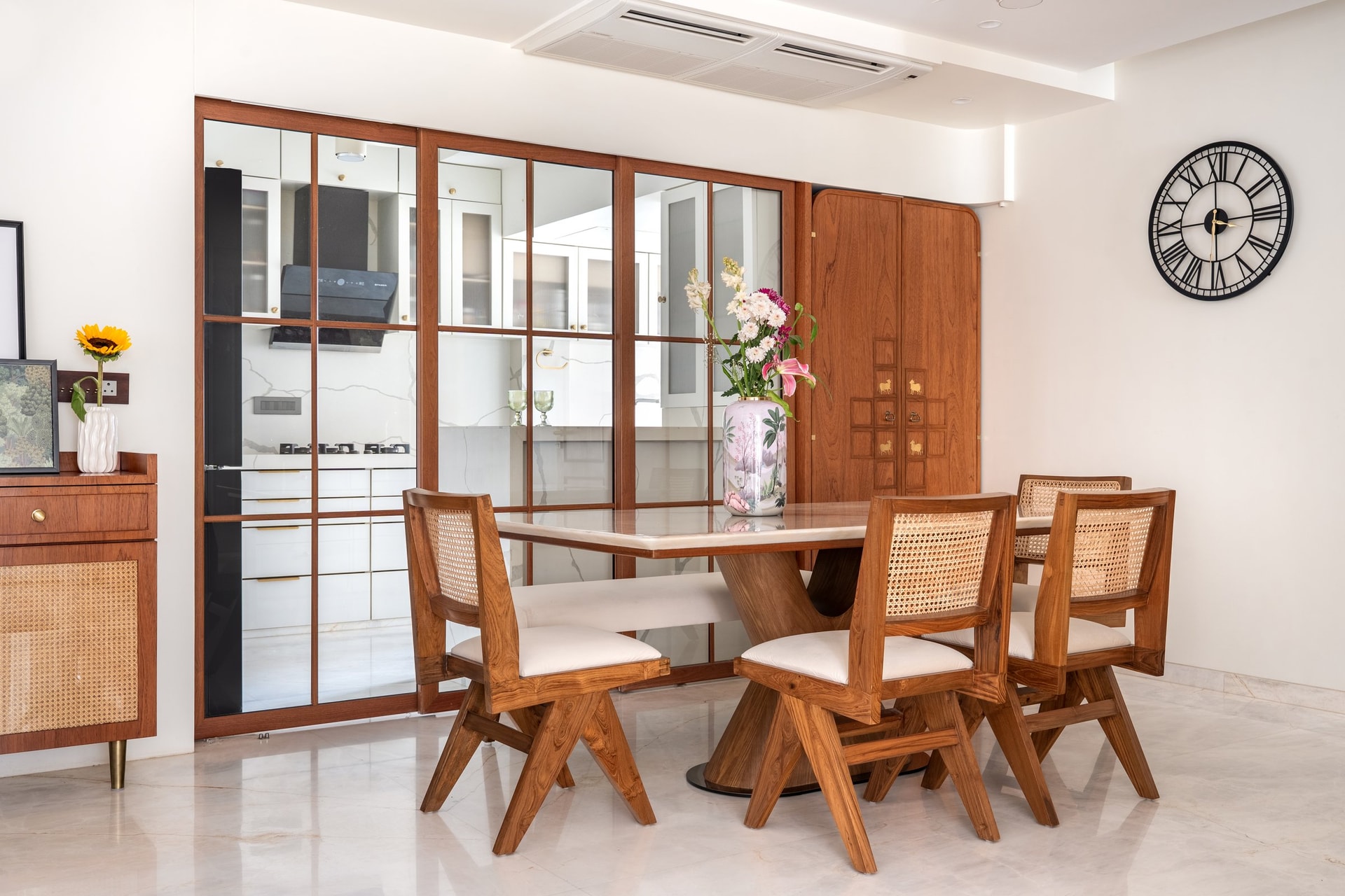 The dining area, screened from the kitchen by a Crittall-style teak partition, with cane-backed chairs around a stone-topped pedestal table