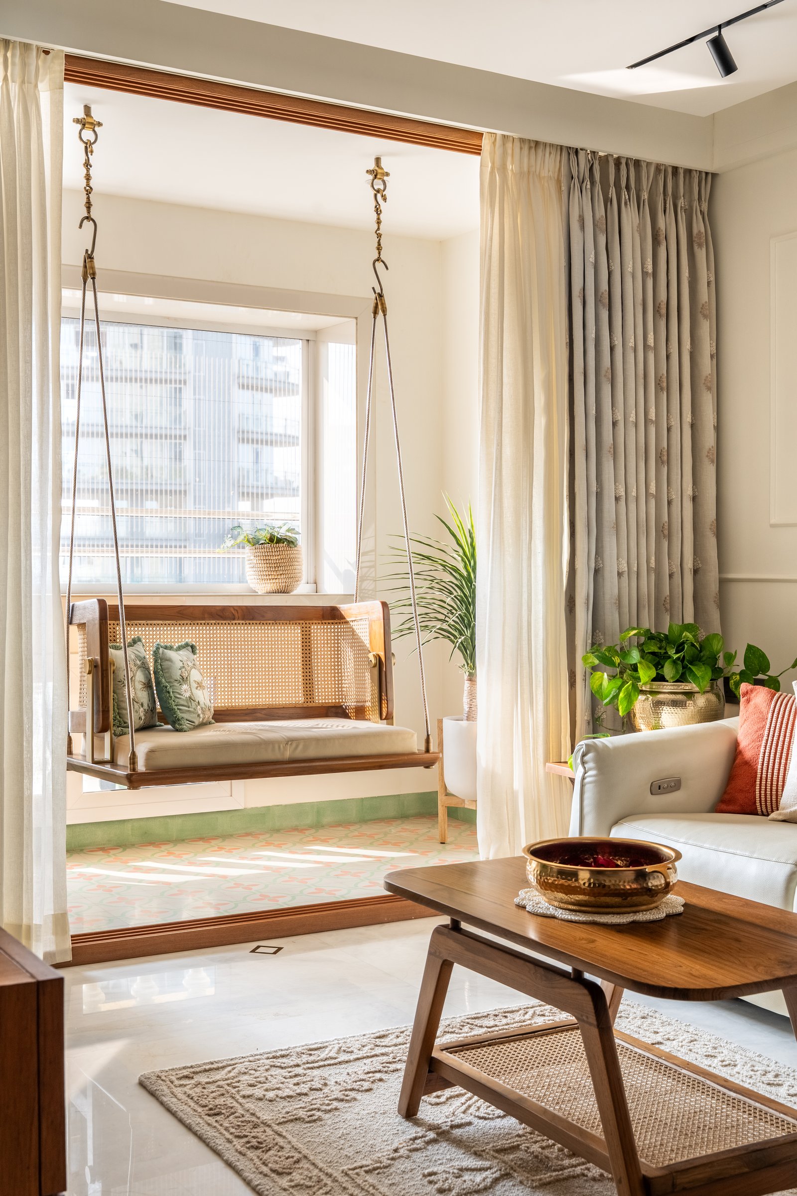 The balcony, where a cane-backed swing on brass hooks lifts just above a patterned tile floor in pale green and coral