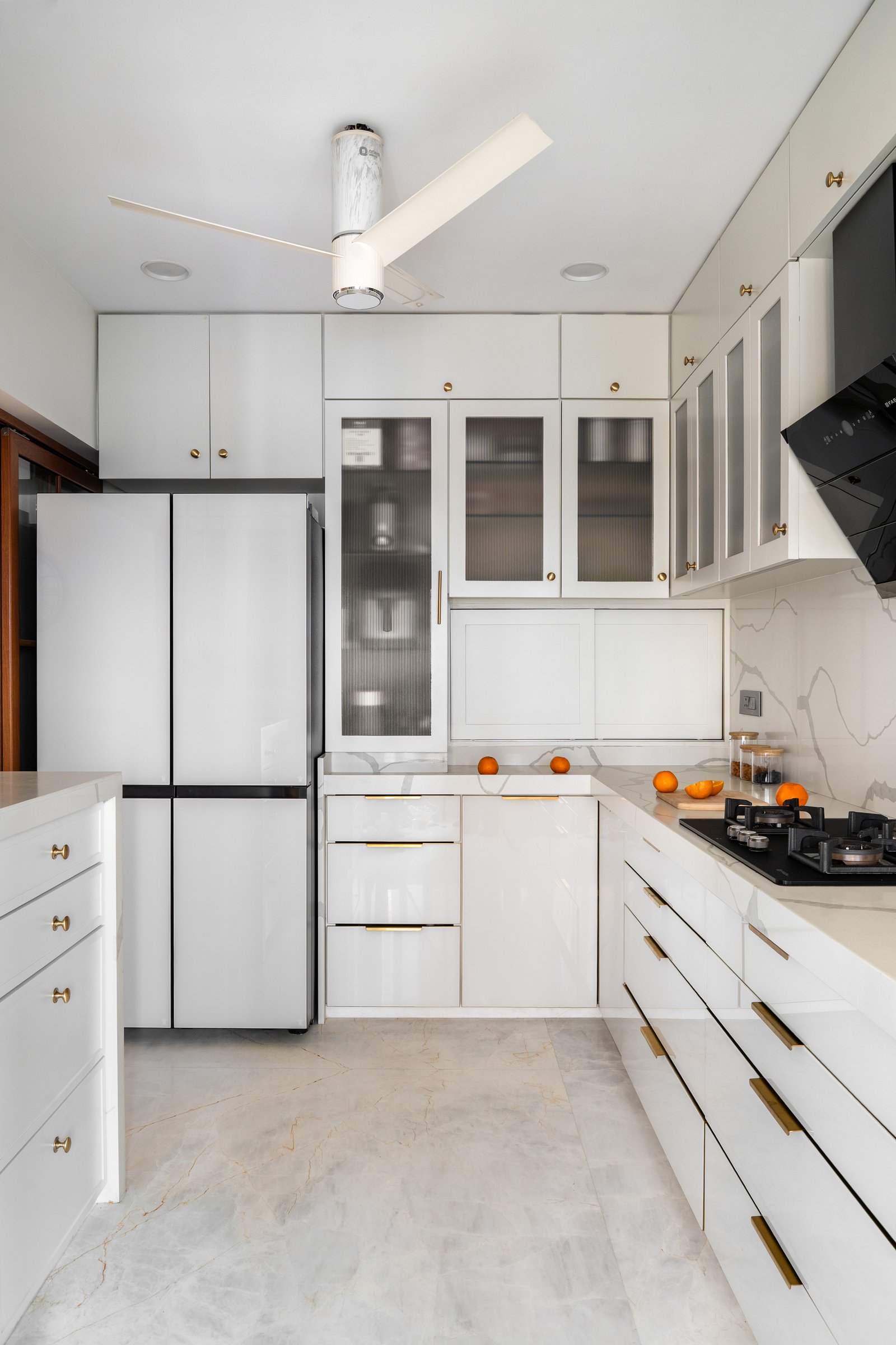 A deeper view of the compact L-shaped kitchen, organised around a tall pantry column and reeded-glass display cabinets