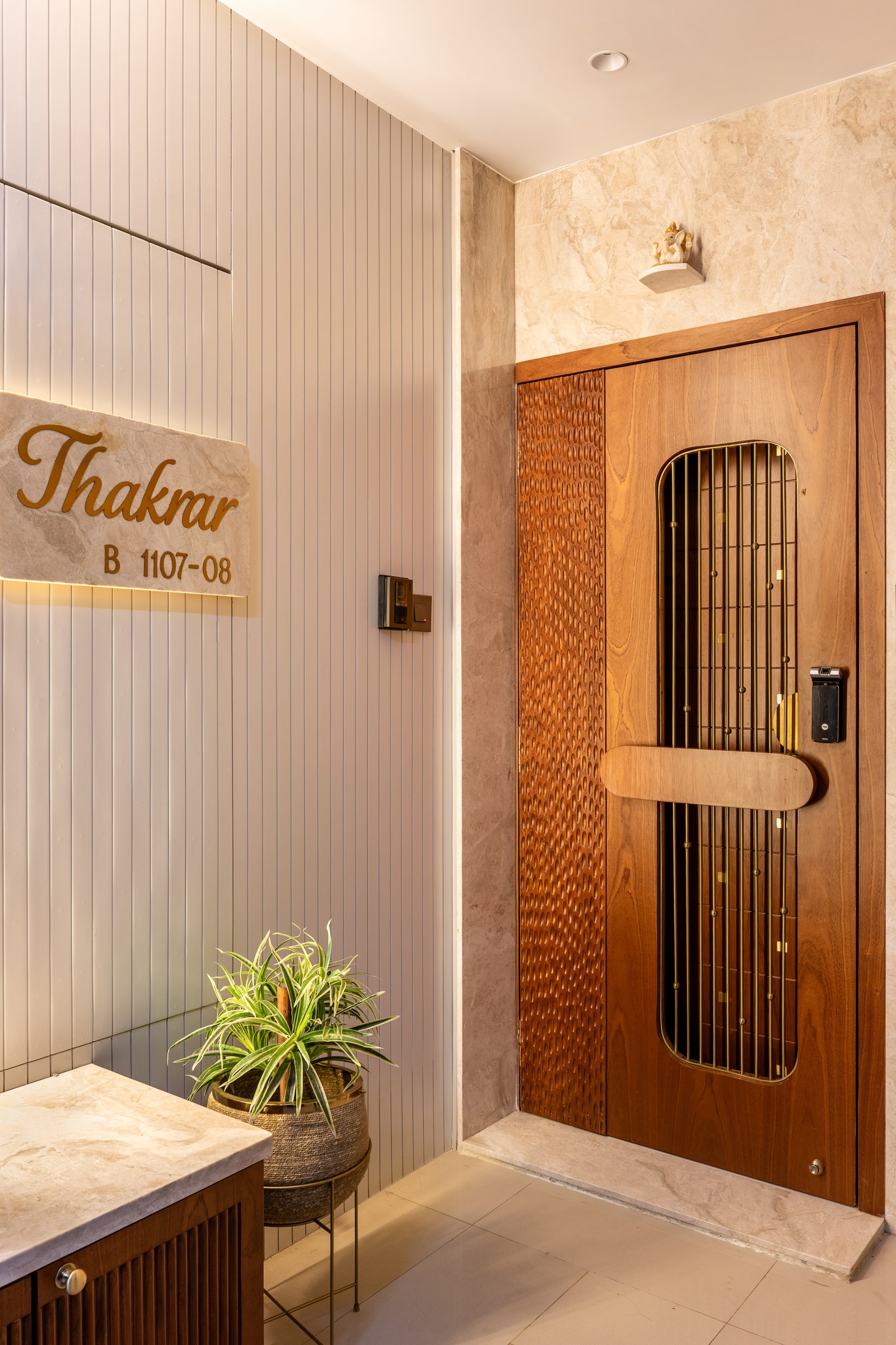 The entry, where a slatted ivory wall meets a warm stone-clad panel and a hammer-detailed teak front door