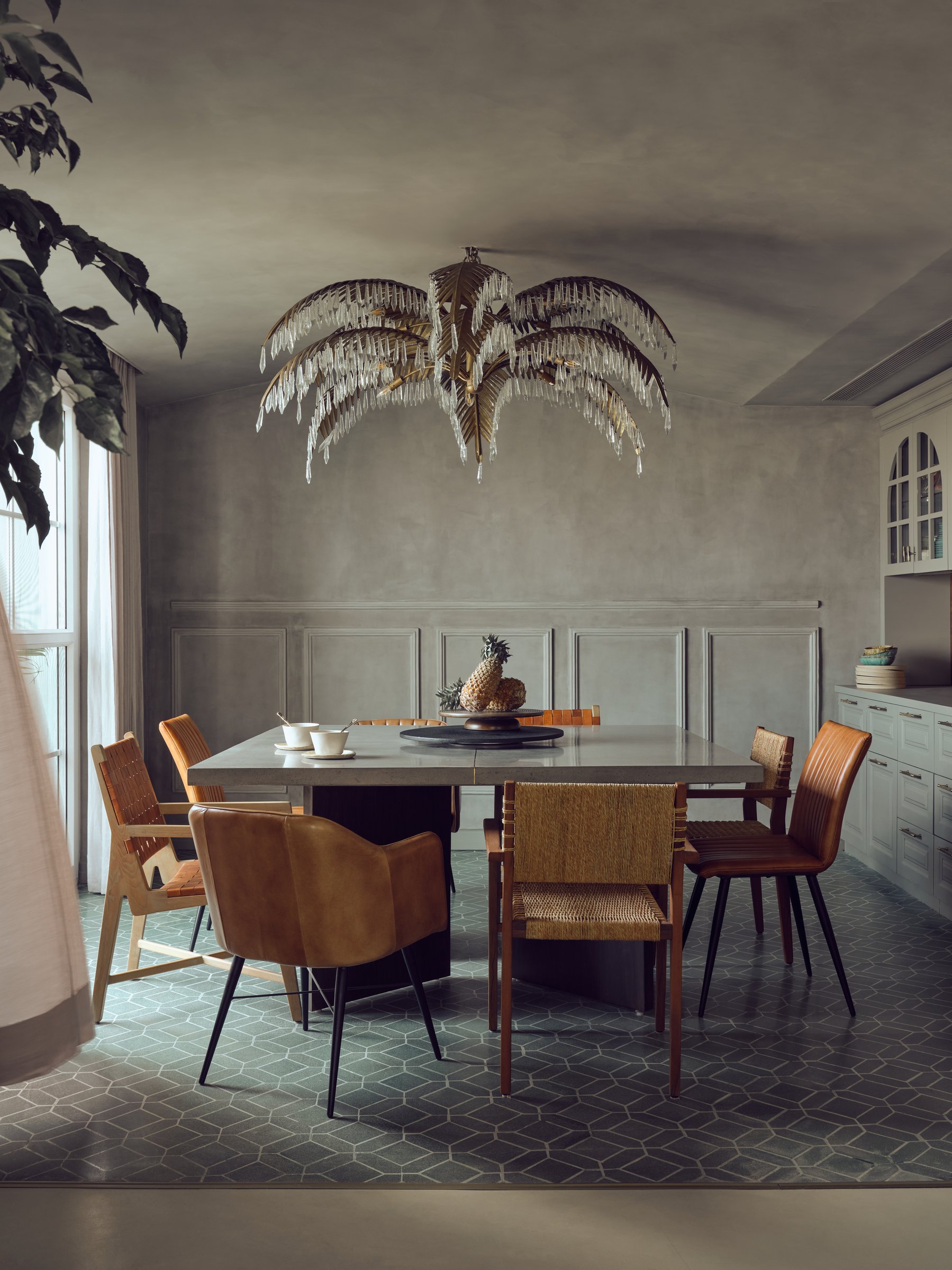 The dining room, where a palm-frond crystal chandelier hovers over a concrete-topped table on green geometric tile