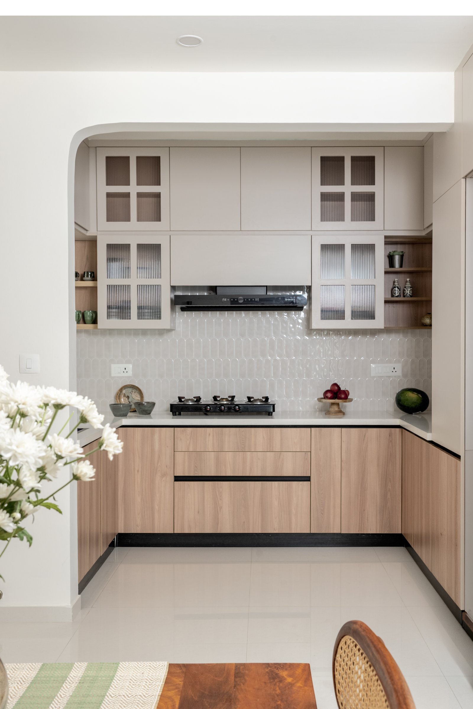 The kitchen framed as a softly arched alcove, with warm wood-grain base cabinets and reeded-glass uppers