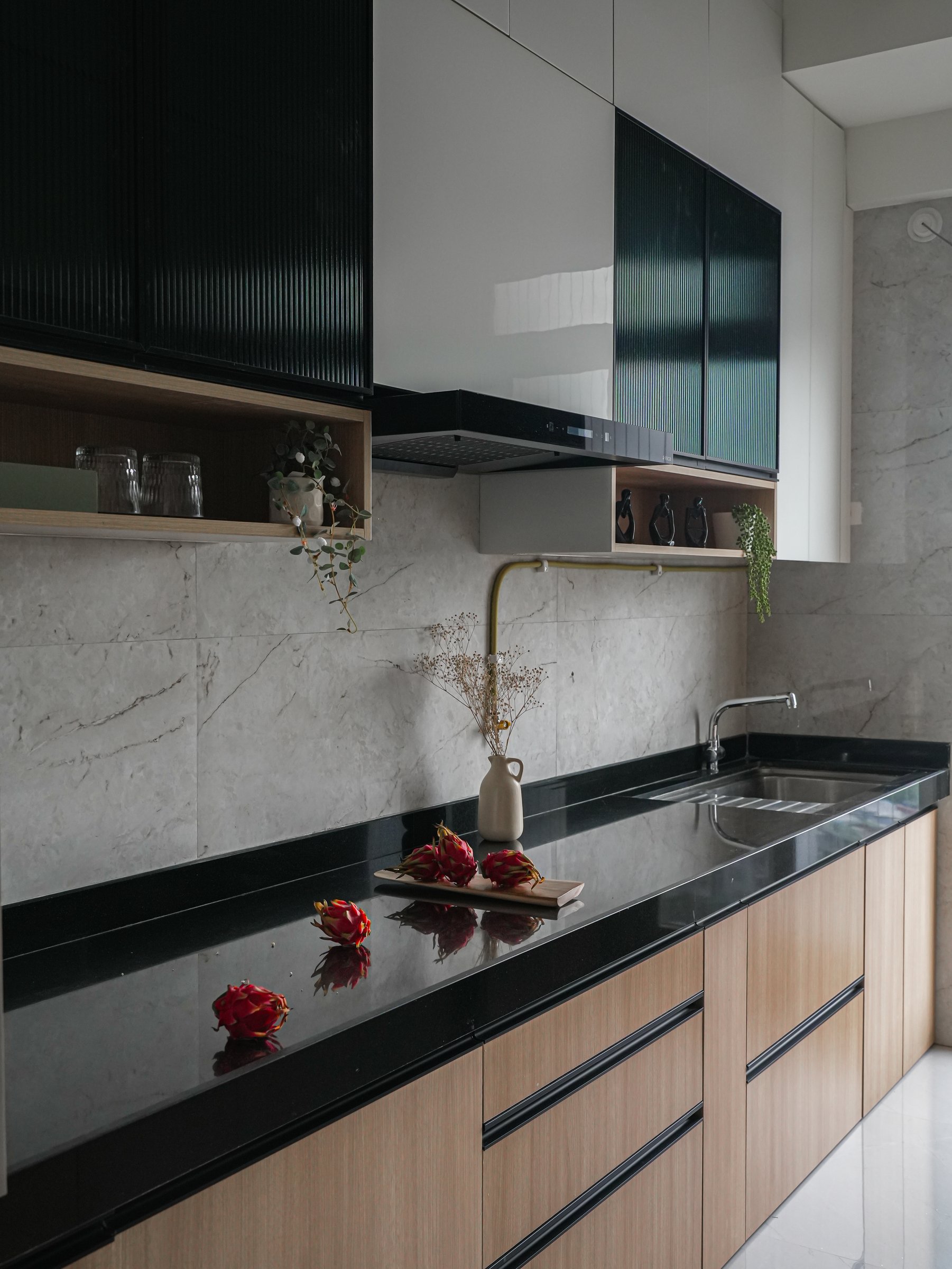 The galley kitchen, where dark stone counters meet warm-toned base cabinetry and reeded dark-glass upper shutters