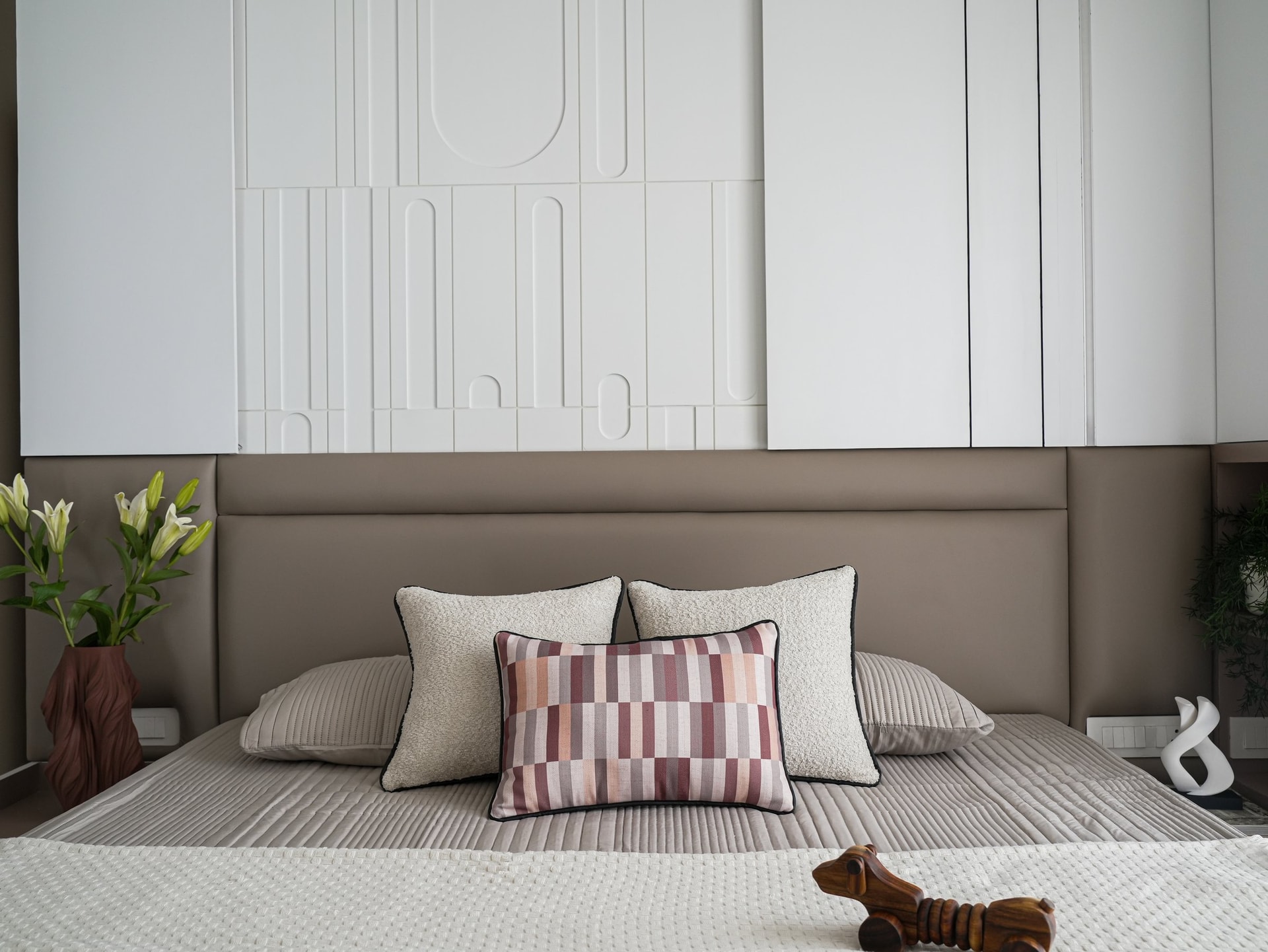 The primary bedroom, where a soft taupe upholstered headboard meets a sculpted white relief panel above