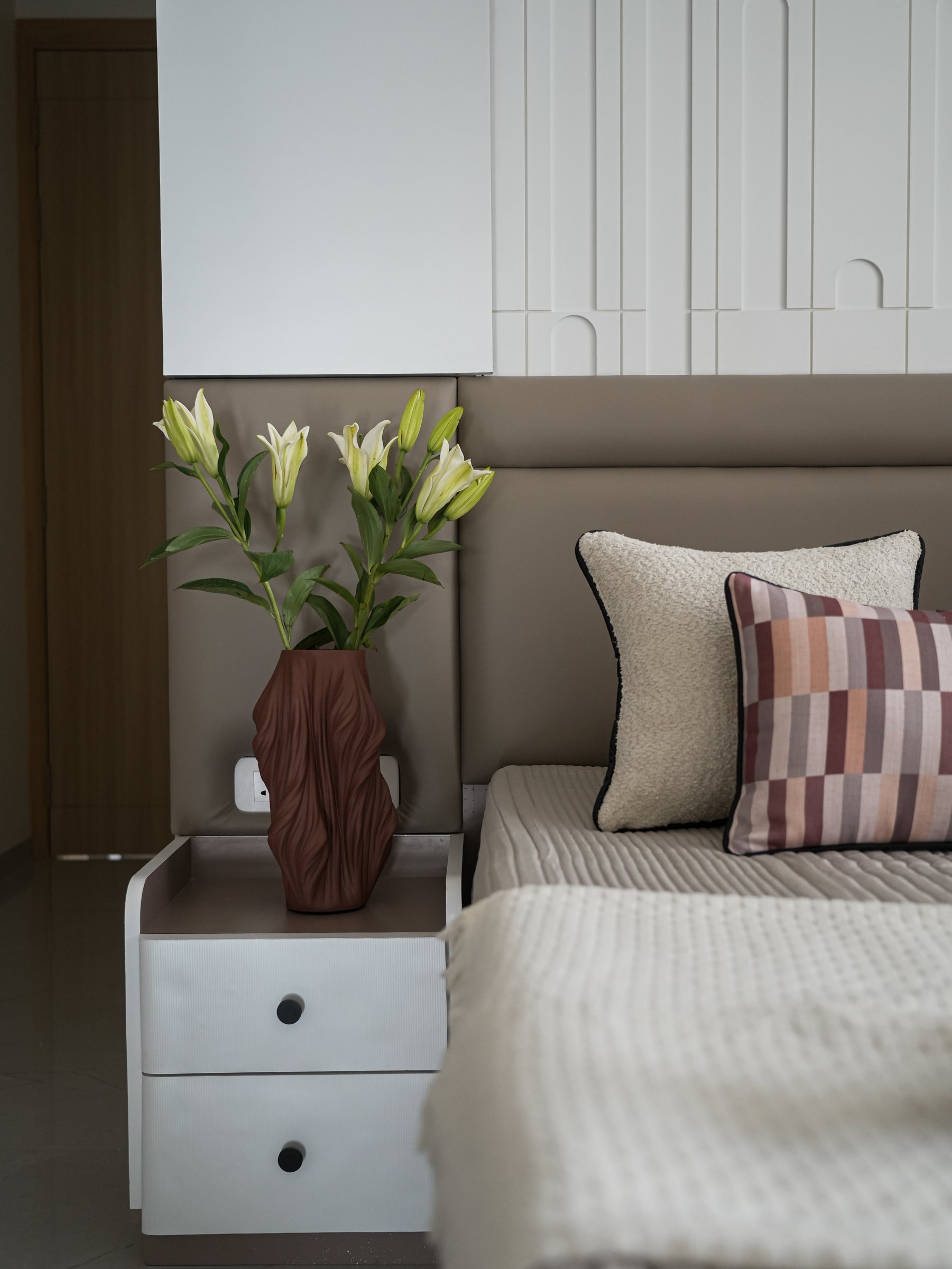 A bedside vignette confirms the room's calibrated register: ribbed drawers, a sculptural terracotta-toned vessel, and fresh lilies