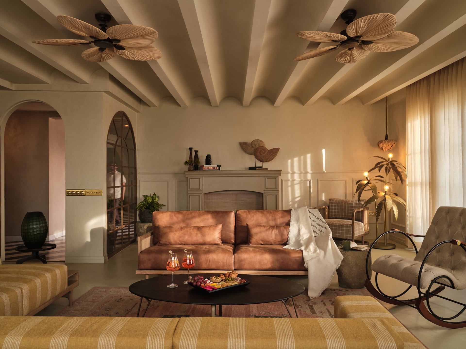 The living room, where a tan leather sofa and scalloped painted beams gather beneath woven ceiling fans