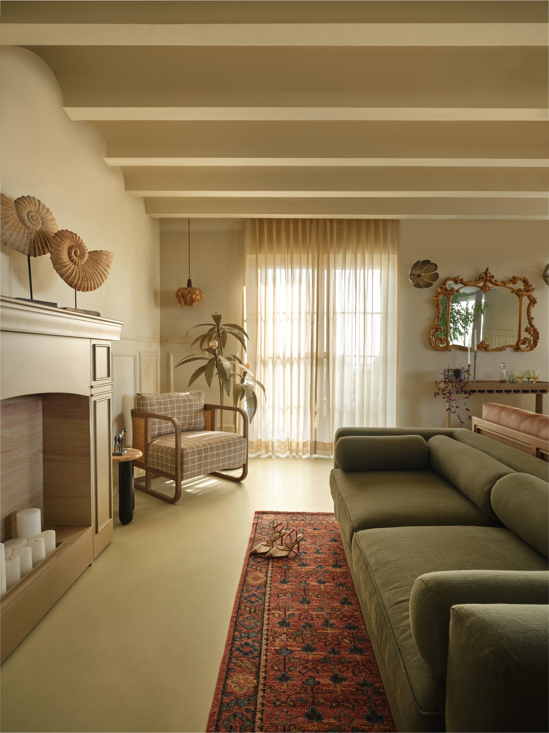 The living room from a second angle, where a green linen sofa faces the fireplace beneath a gilded mirror