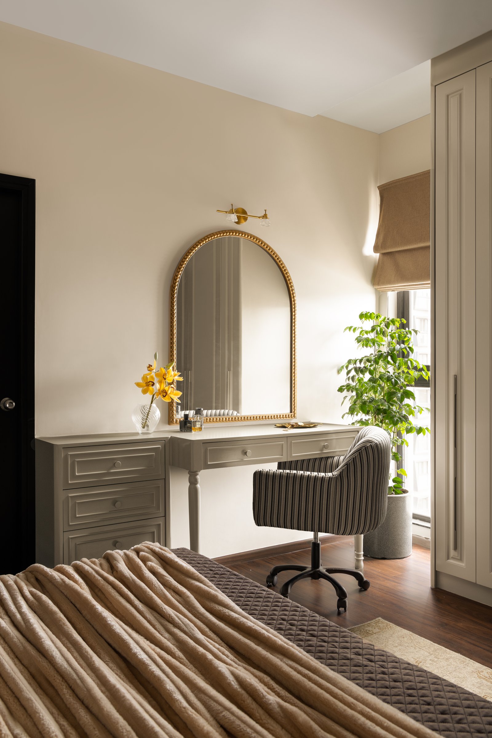A dressing corner with a gold-rimmed arched mirror, catching morning light beside the window