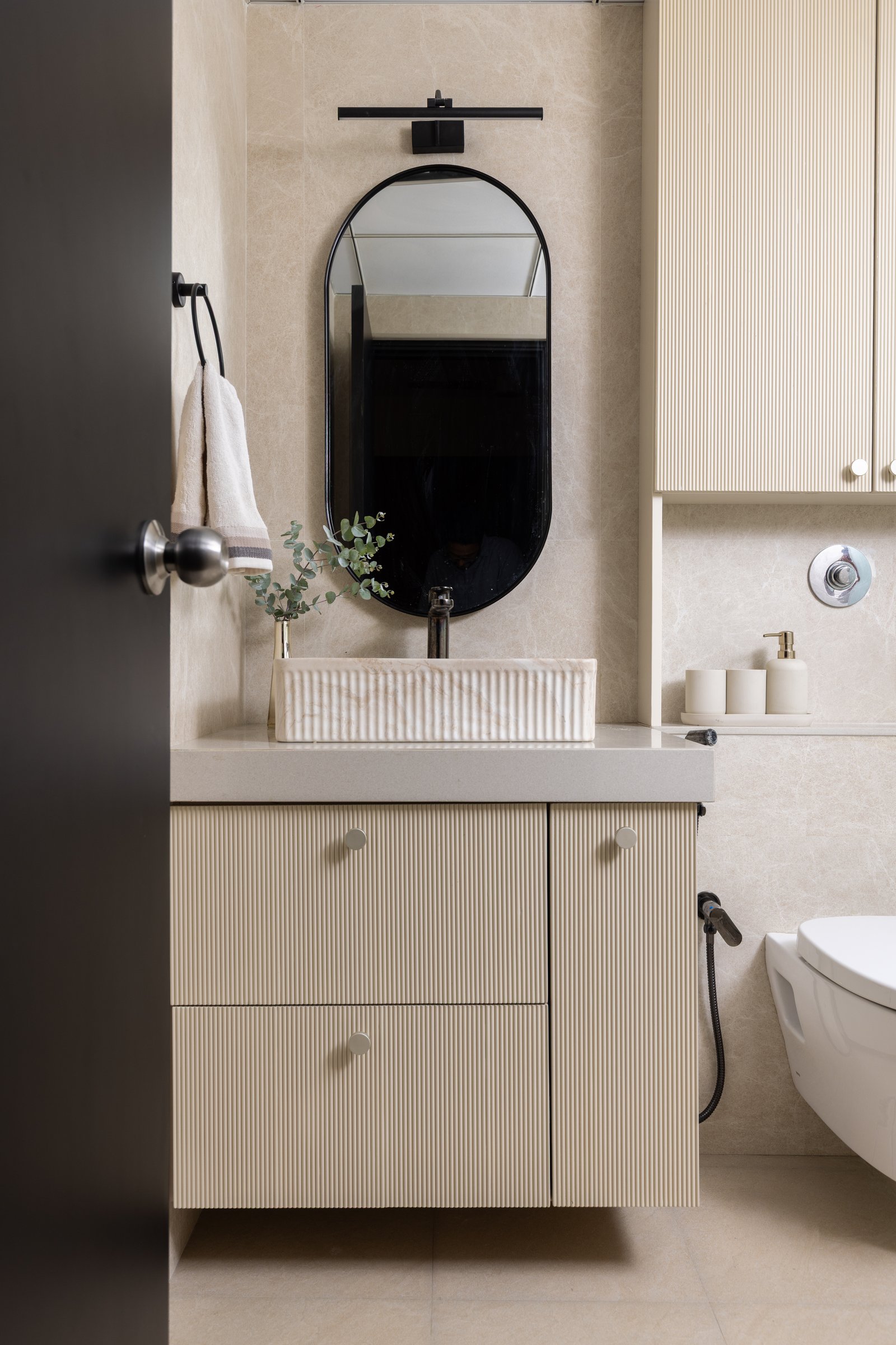 The master bathroom, where fluted stone and cabinetry translate the bedroom’s hush