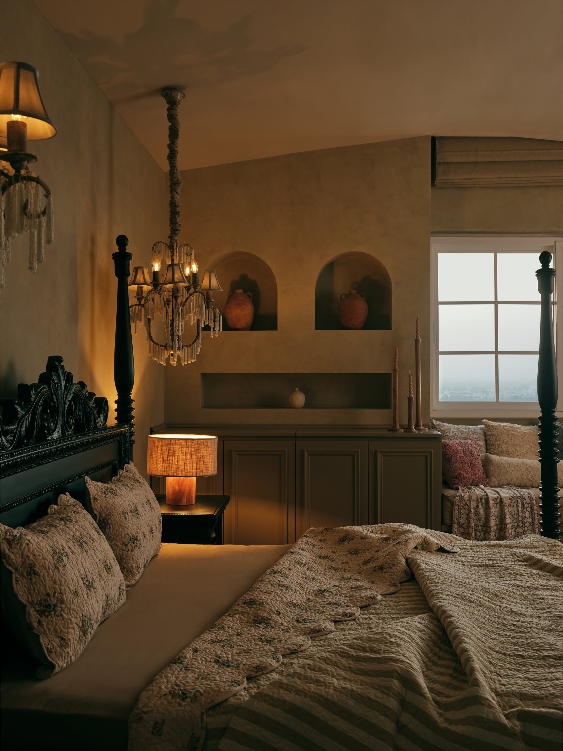 The master bedroom, where lime-washed walls, arched niches, and a dark four-poster hold the home's most intimate register