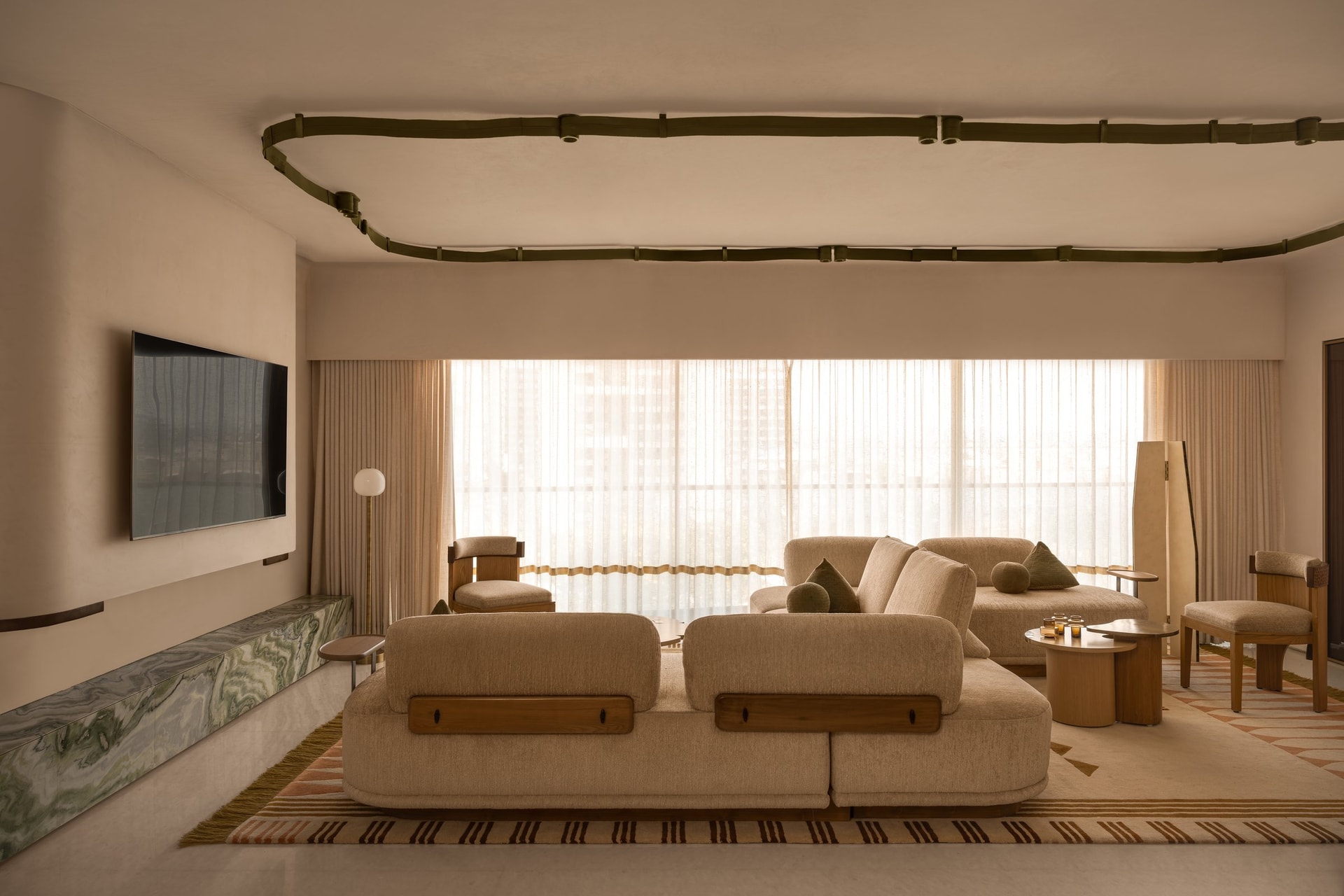 The living room, where a serpentine ceiling detail traces the gesture of an unfurling ribbon above a palette of soft neutrals and muted green
